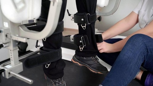 close-up of a doctor's hands adjusting a rehabilitation machine to a child patient on her legs