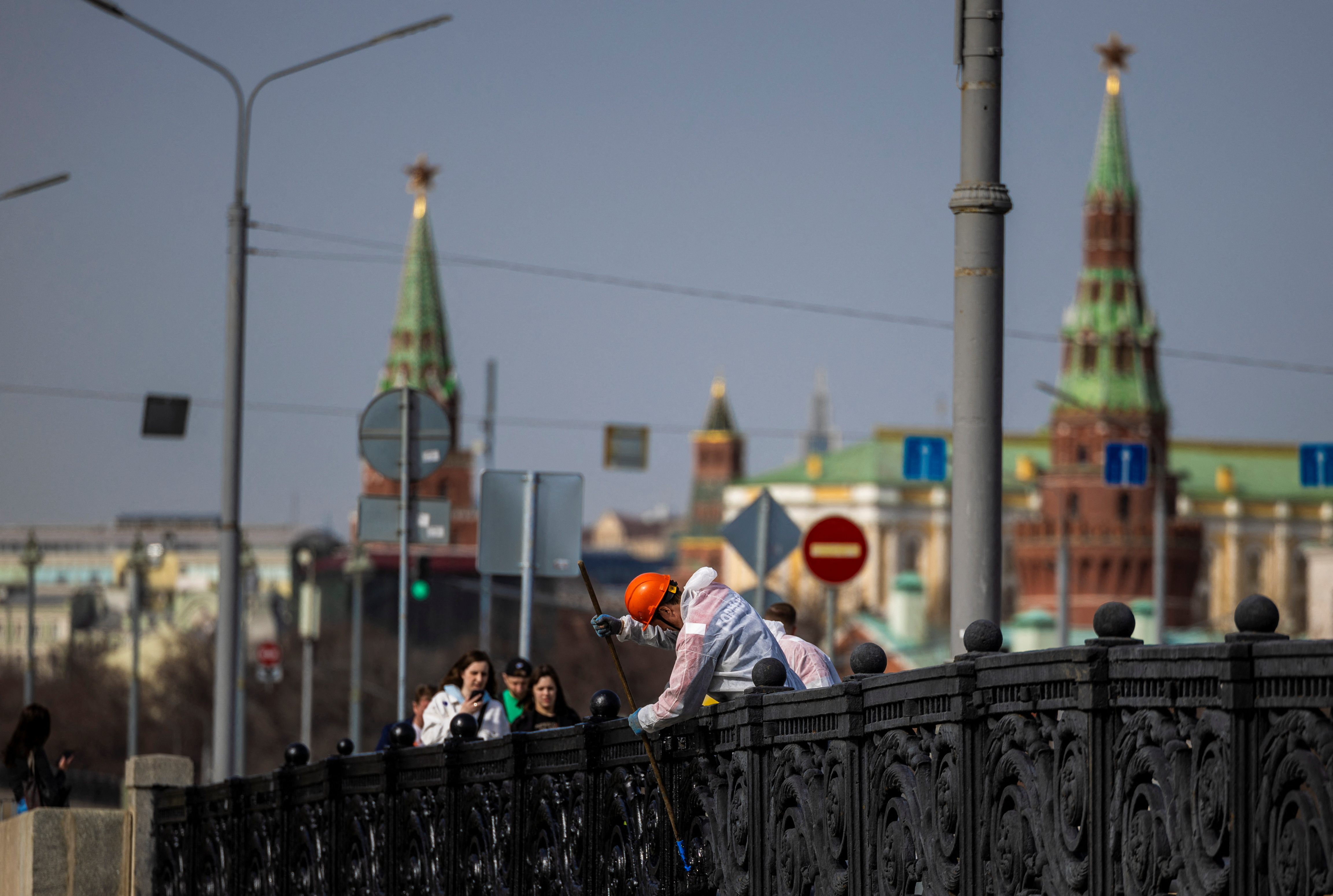 A communal worker paints a fence on a bridge in Moscow