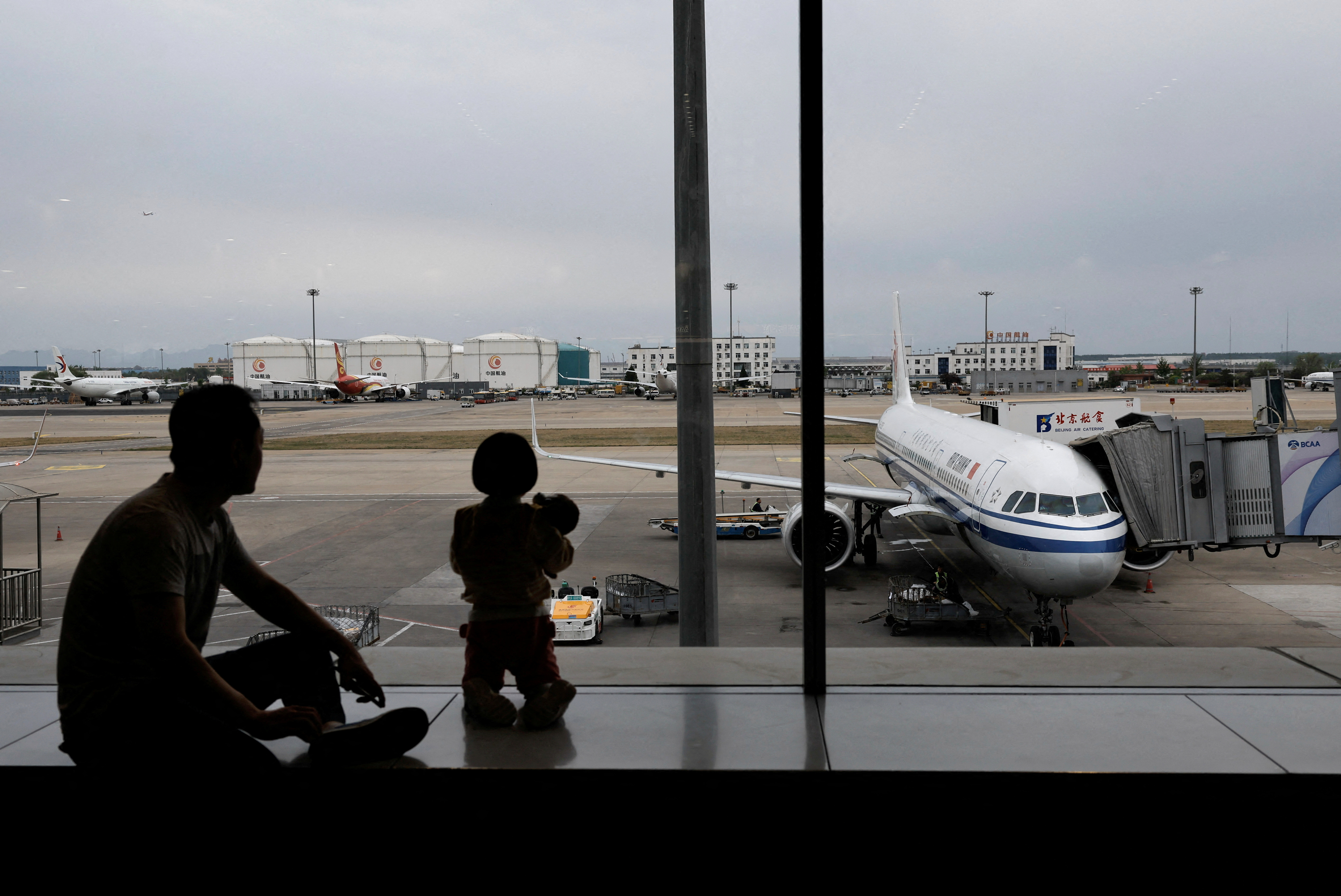 Passengers look at the tarmac as they wait for their flights at the Beijing Capital International Airport, in Beijing