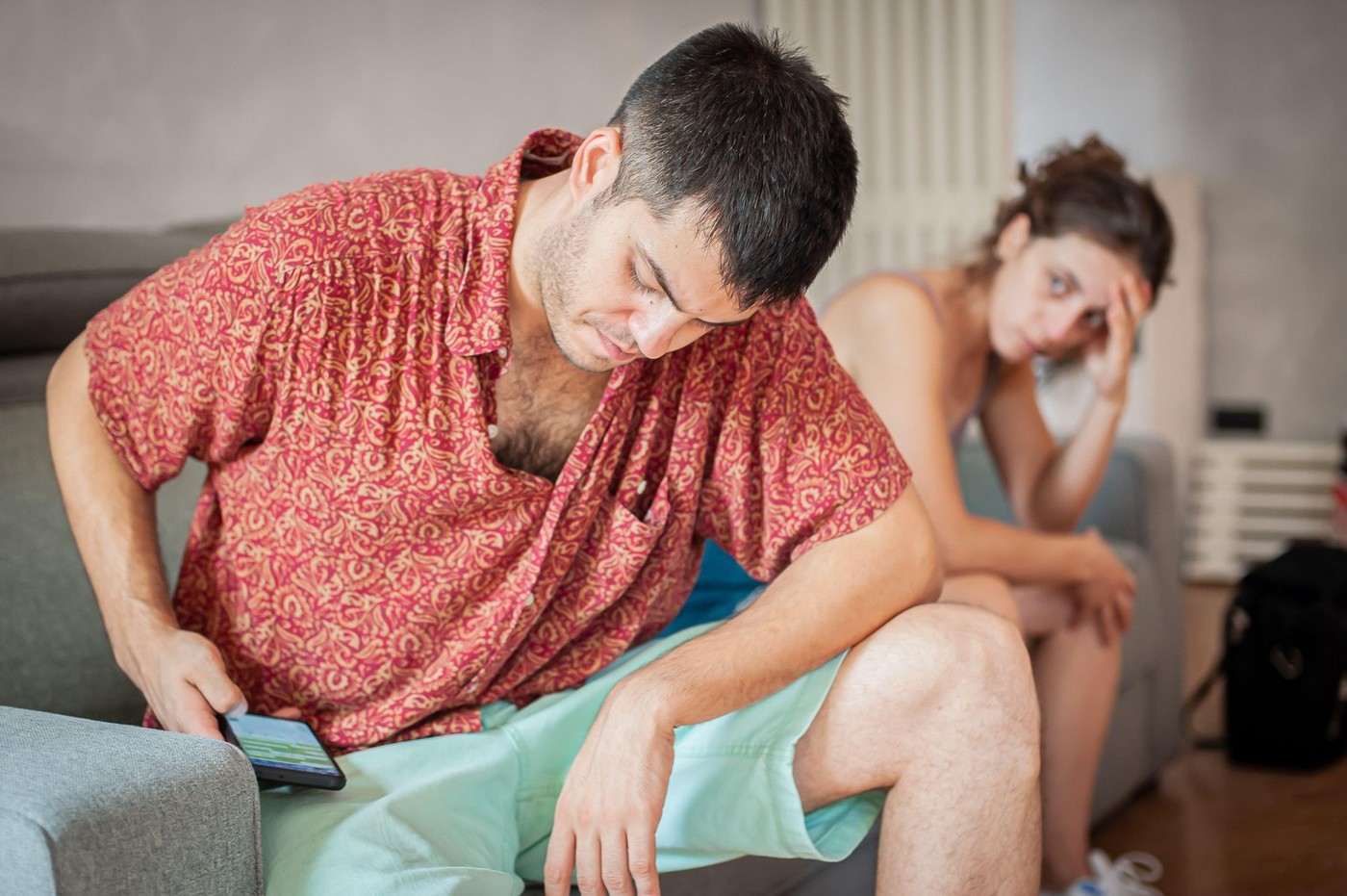 A young sad woman is next to her partner who is texting on the phone with someone, and not paying attention to her.