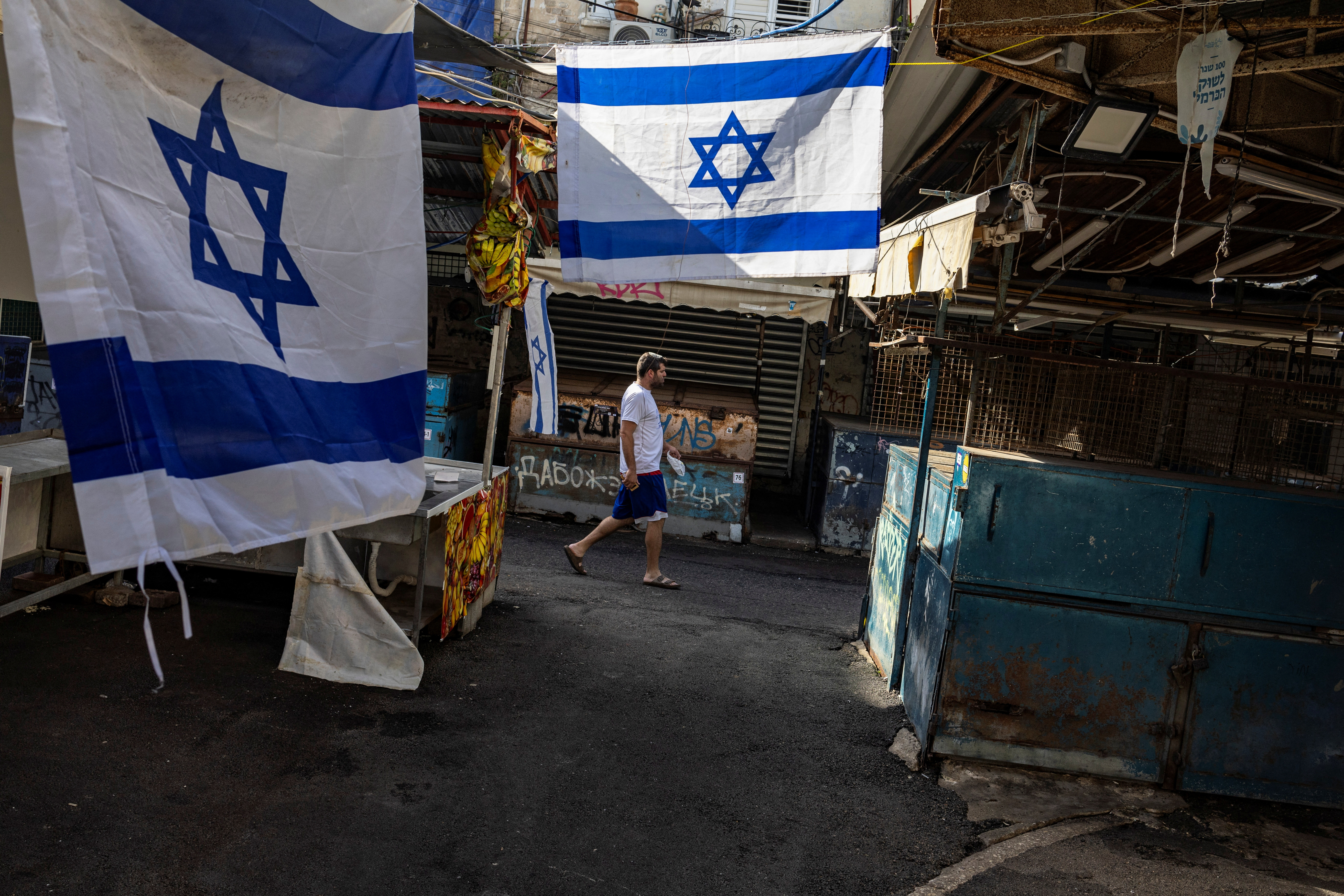 A man walks past Israeli flags at the green market, in Tel Aviv