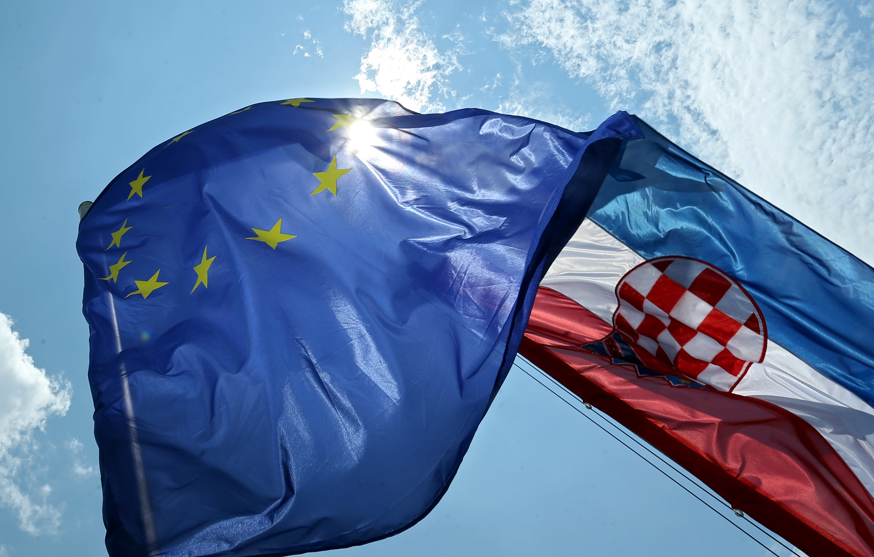 Zastave Hrvatske i Europske unije podignute prema vedrom nebu i suncu