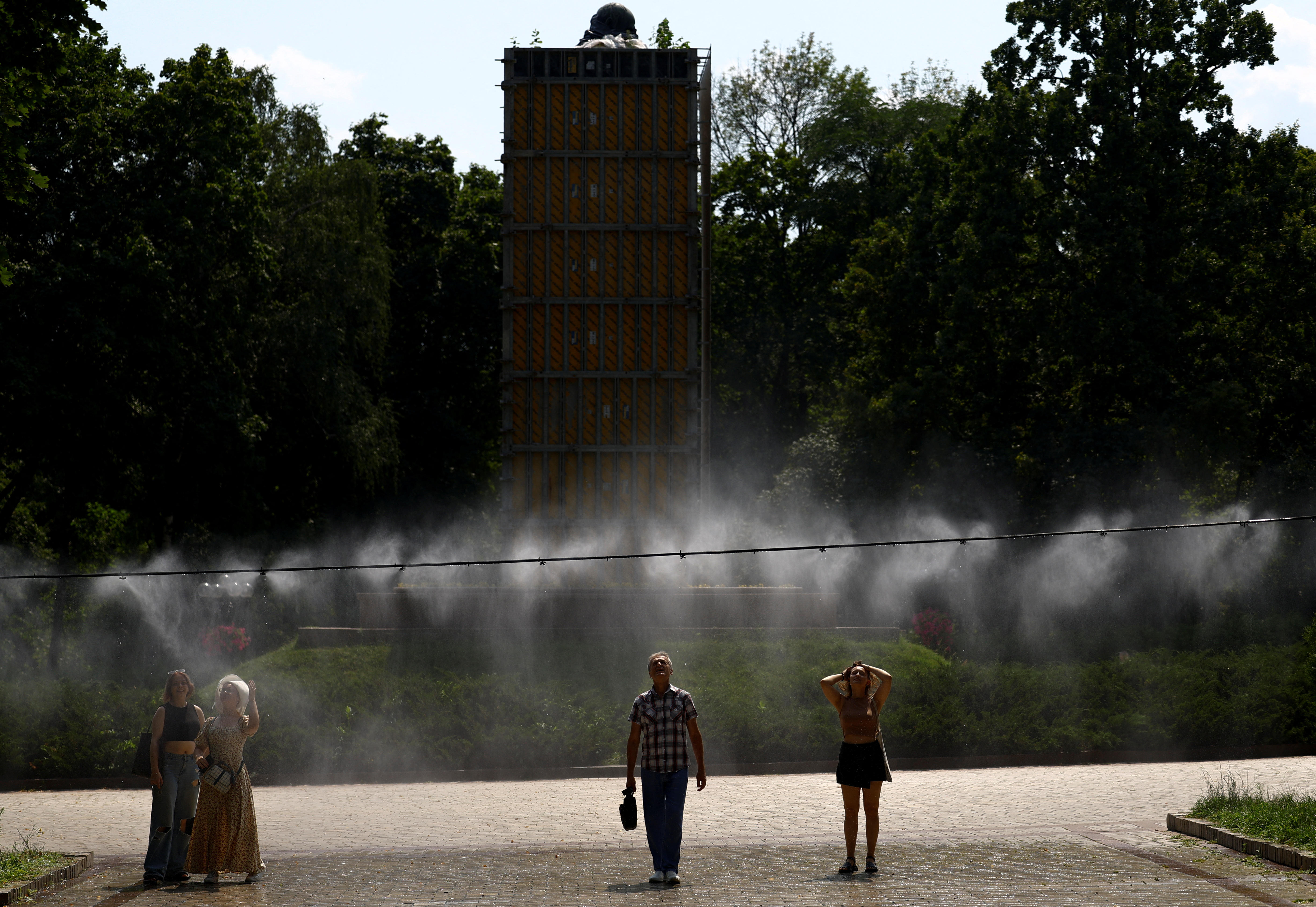 People cool themselves under a water sprinkler on an extremely hot summer day in Kyiv