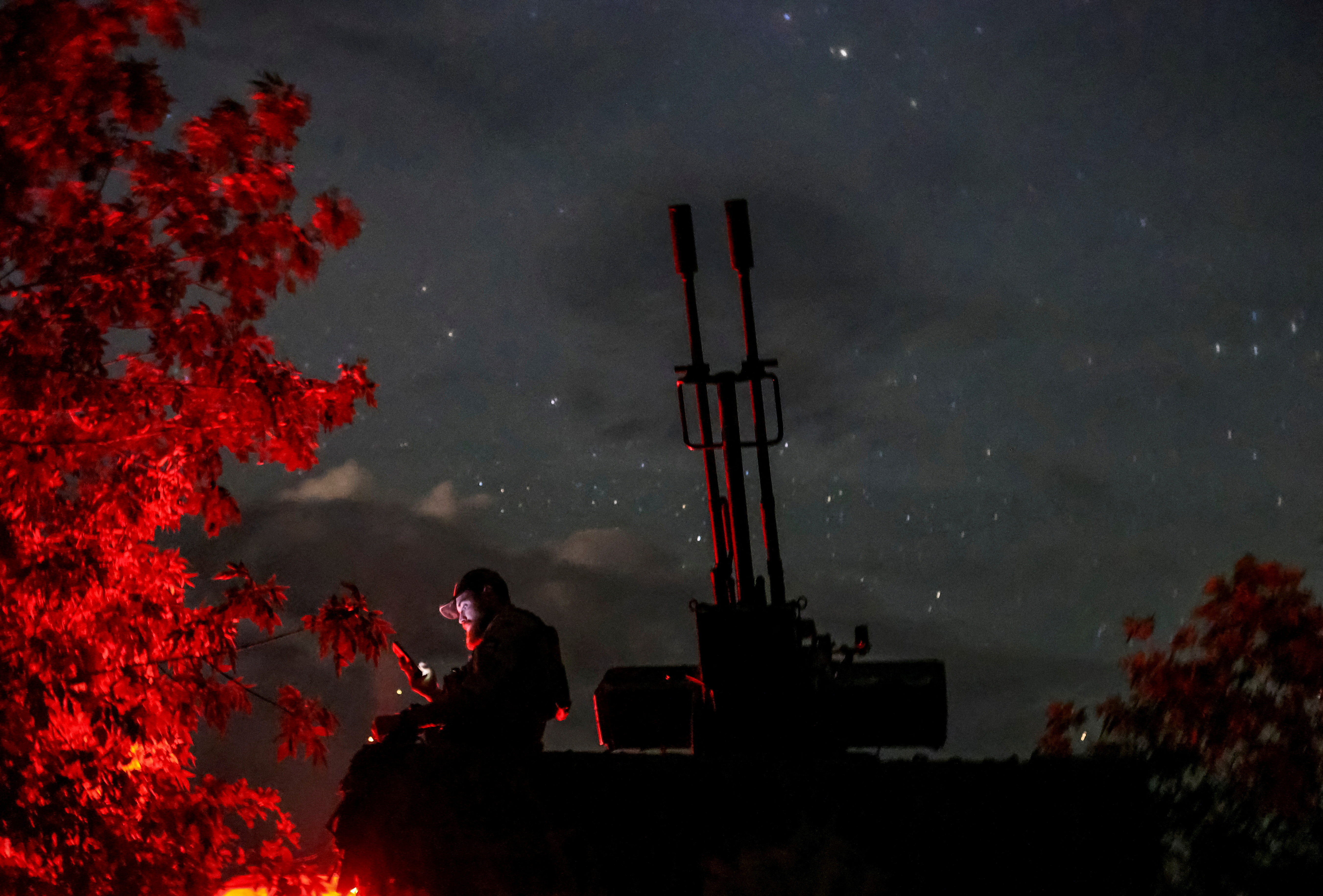 FILE PHOTO: A Ukrainian serviceman from an anti-drone mobile air defence unit uses his mobile device near an anti aircraft cannon as he waits for Russian kamikaze drones in Kherson region