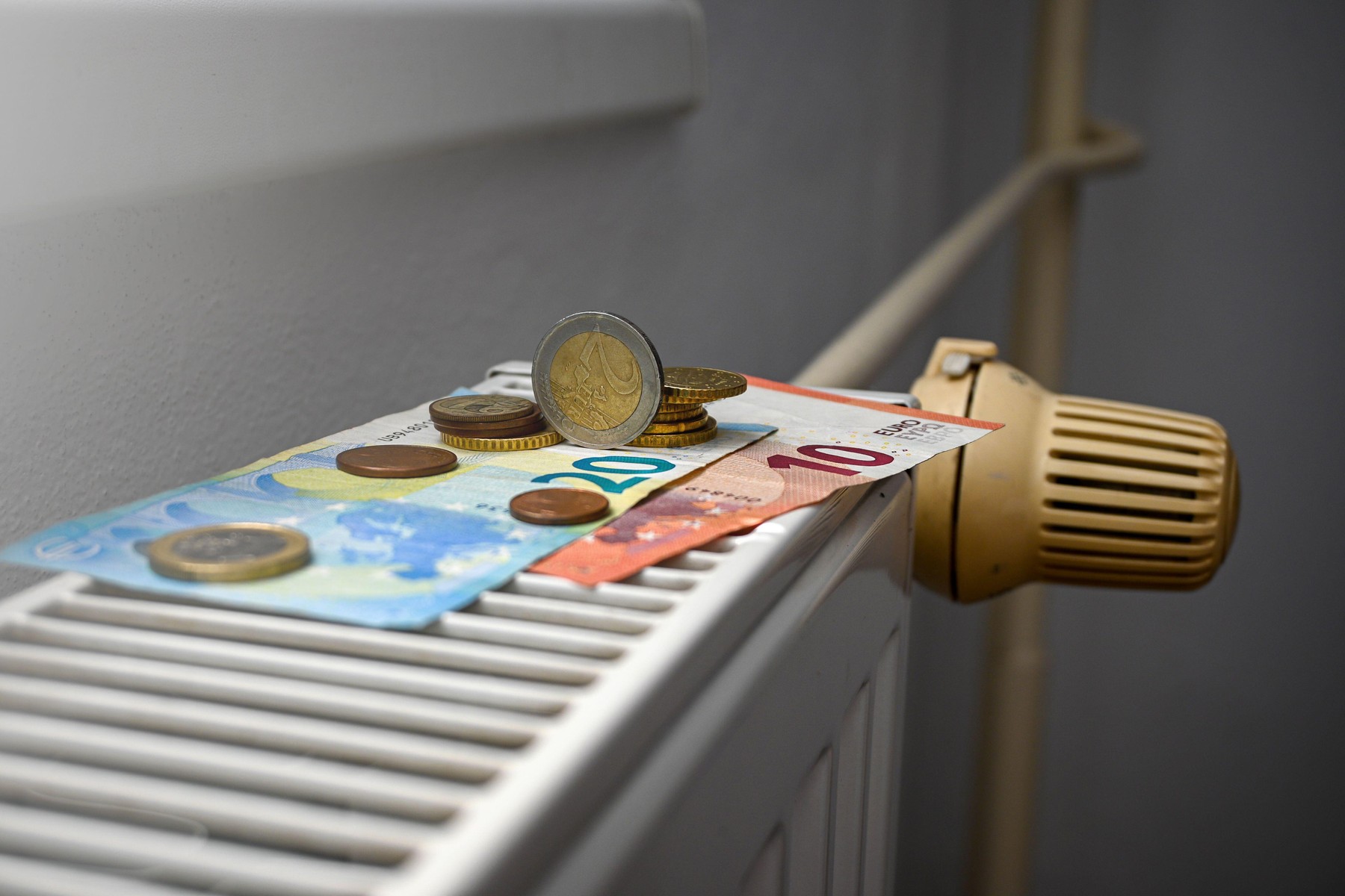Euro banknotes and coins are sitting on a radiator, illustrating the increasing cost of heating.