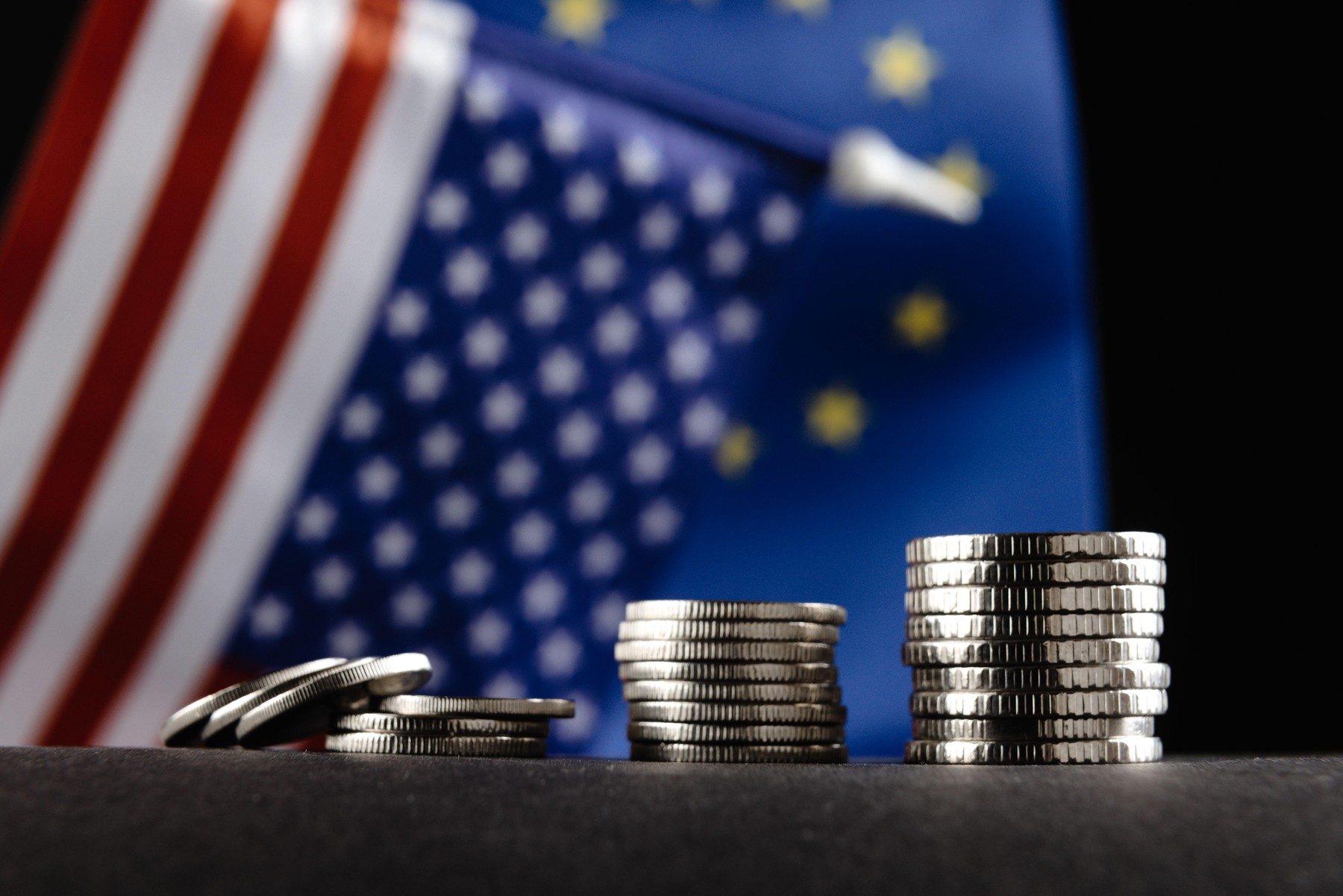 Money of the United States and Europe and two Flags on a dark background. It is a symbol of the United States of America increasing tariff tax