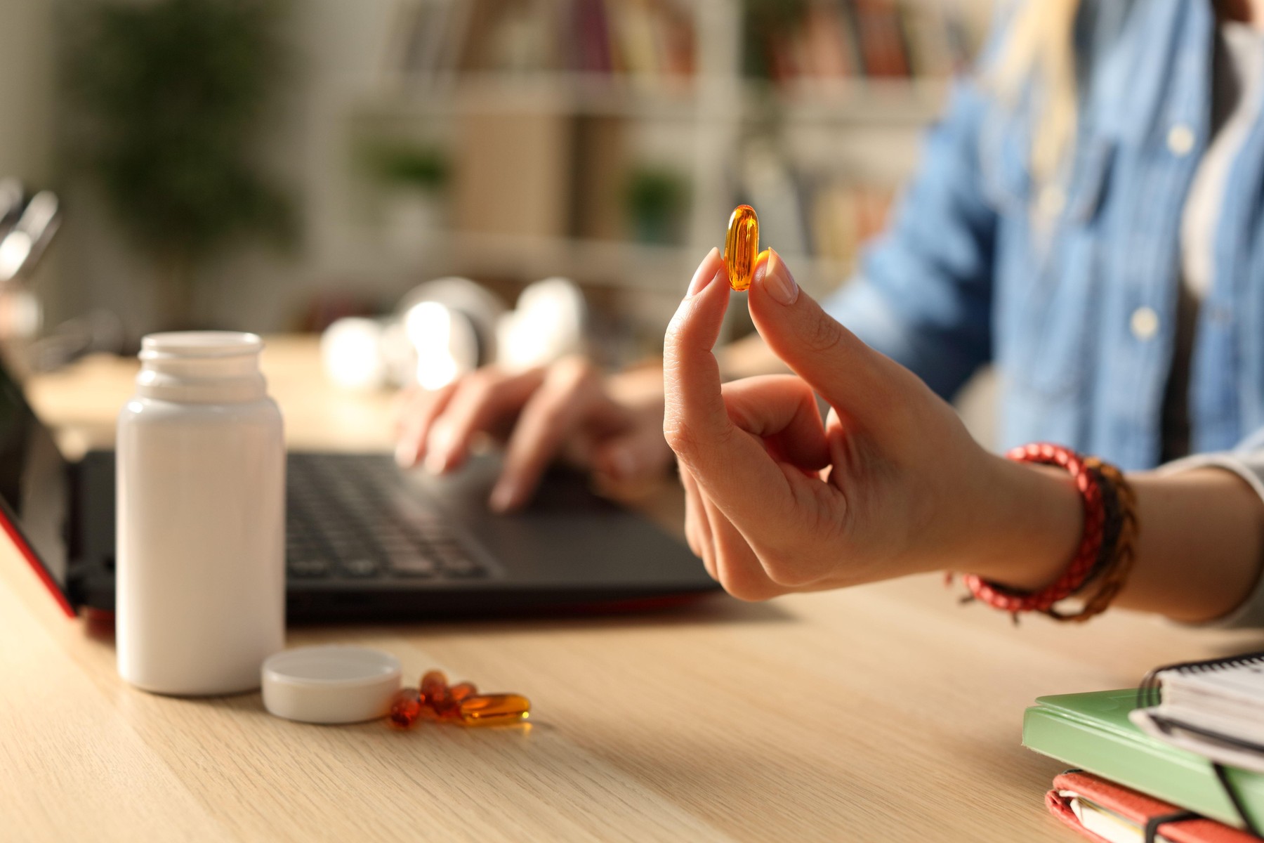 Close up of student girl hand studying showing vitamine pill at night sitting on a desk at home