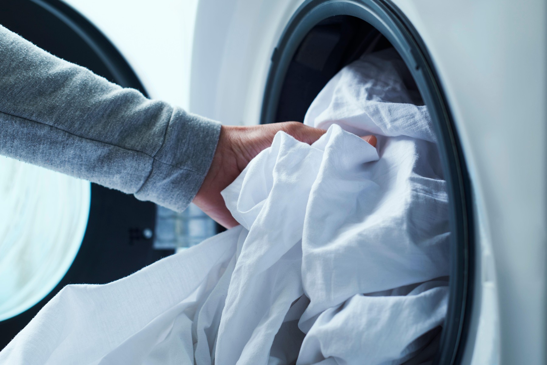 closeup of a young caucasian man putting white bed linen into the washing machine
