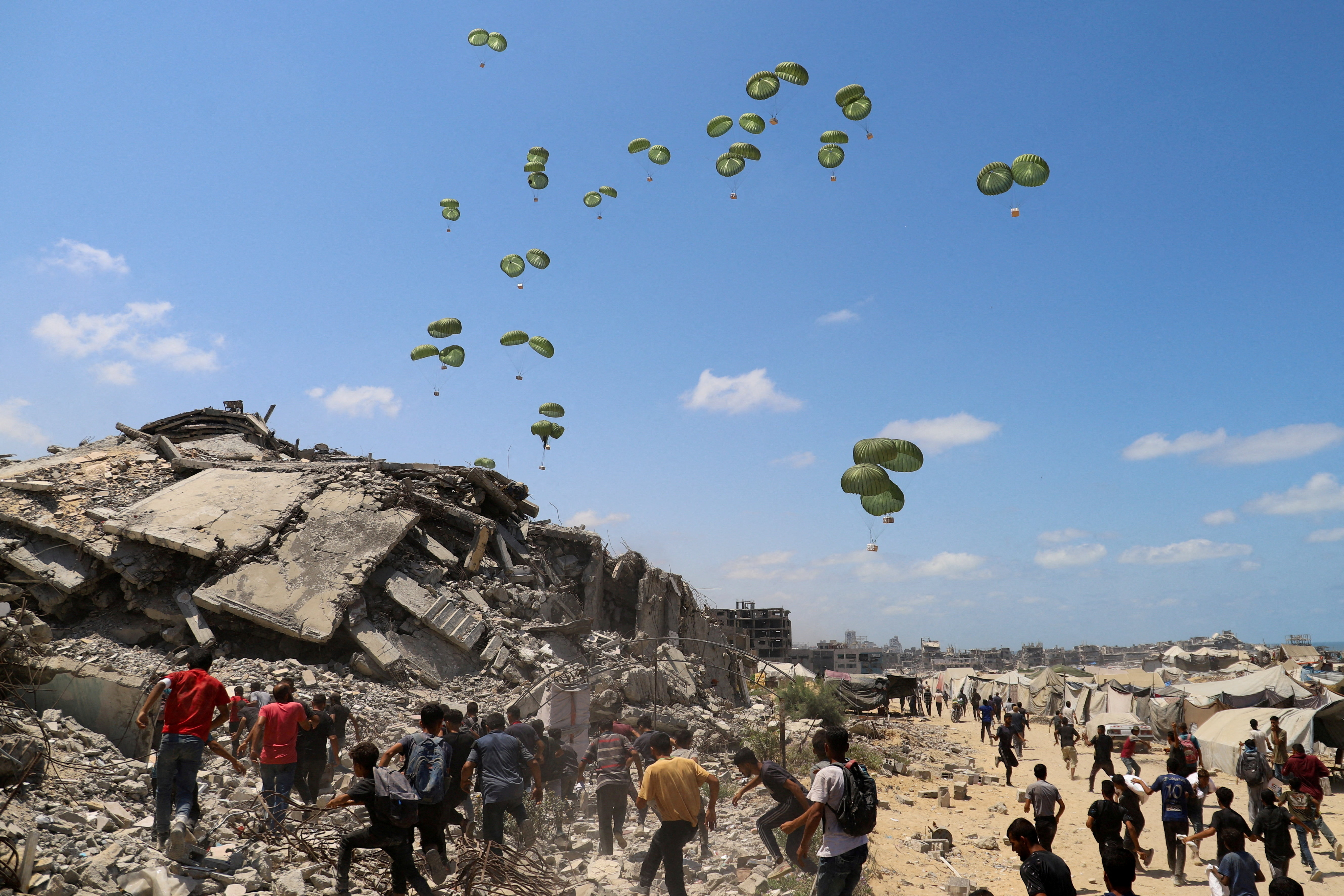 FILE PHOTO: Palestinians run towards parachutes carrying aid packages airdropped over northern Gaza Strip, August 7, 2025. REUTERS/Ebrahim Hajjaj/File Photo