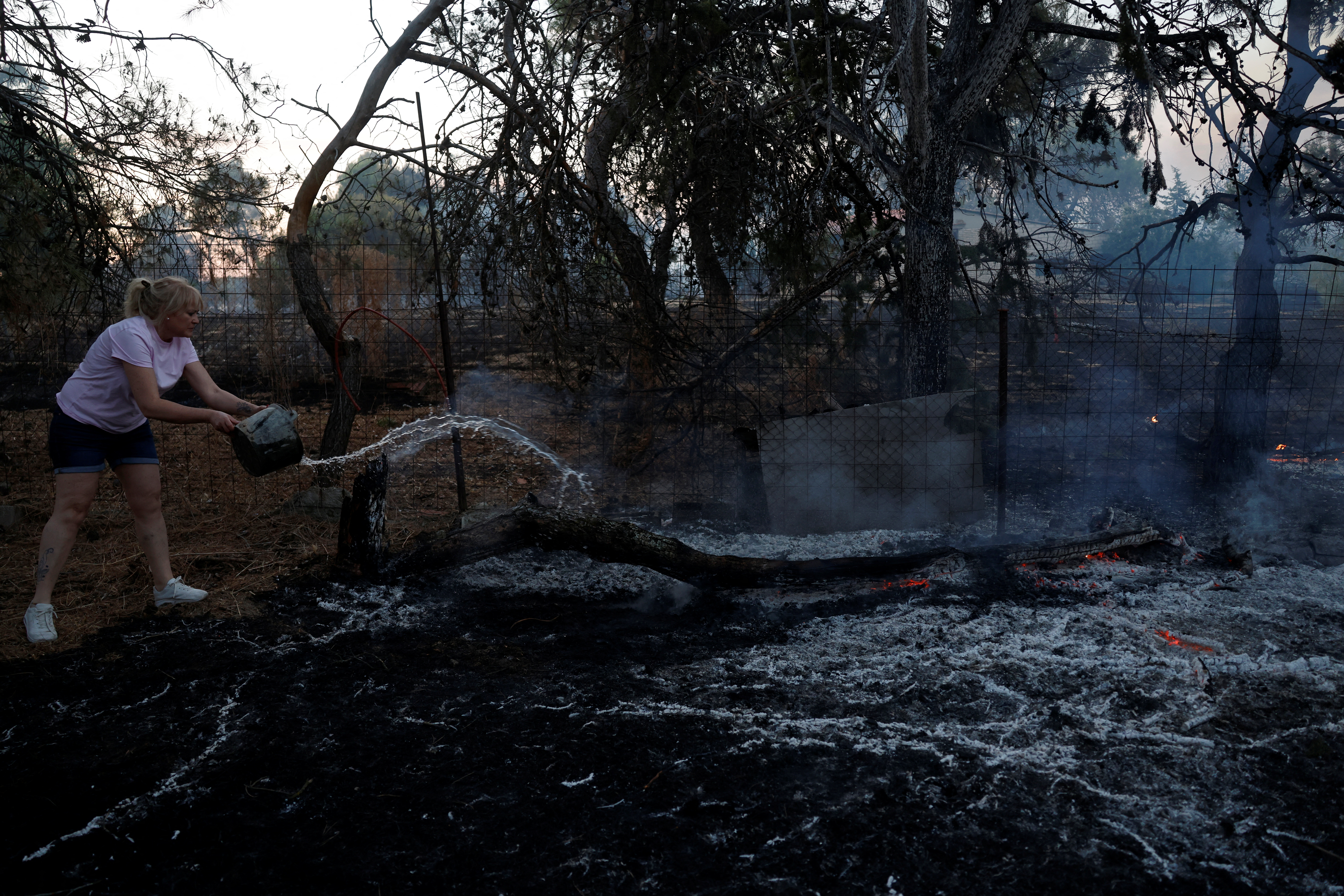 Maria Carmen Herraiz pours water from a bucket to put out a fire at a home garden as a wildfire rages on the outskirts of Valmojado, Spain, July 17, 2025. REUTERS/Susana Vera