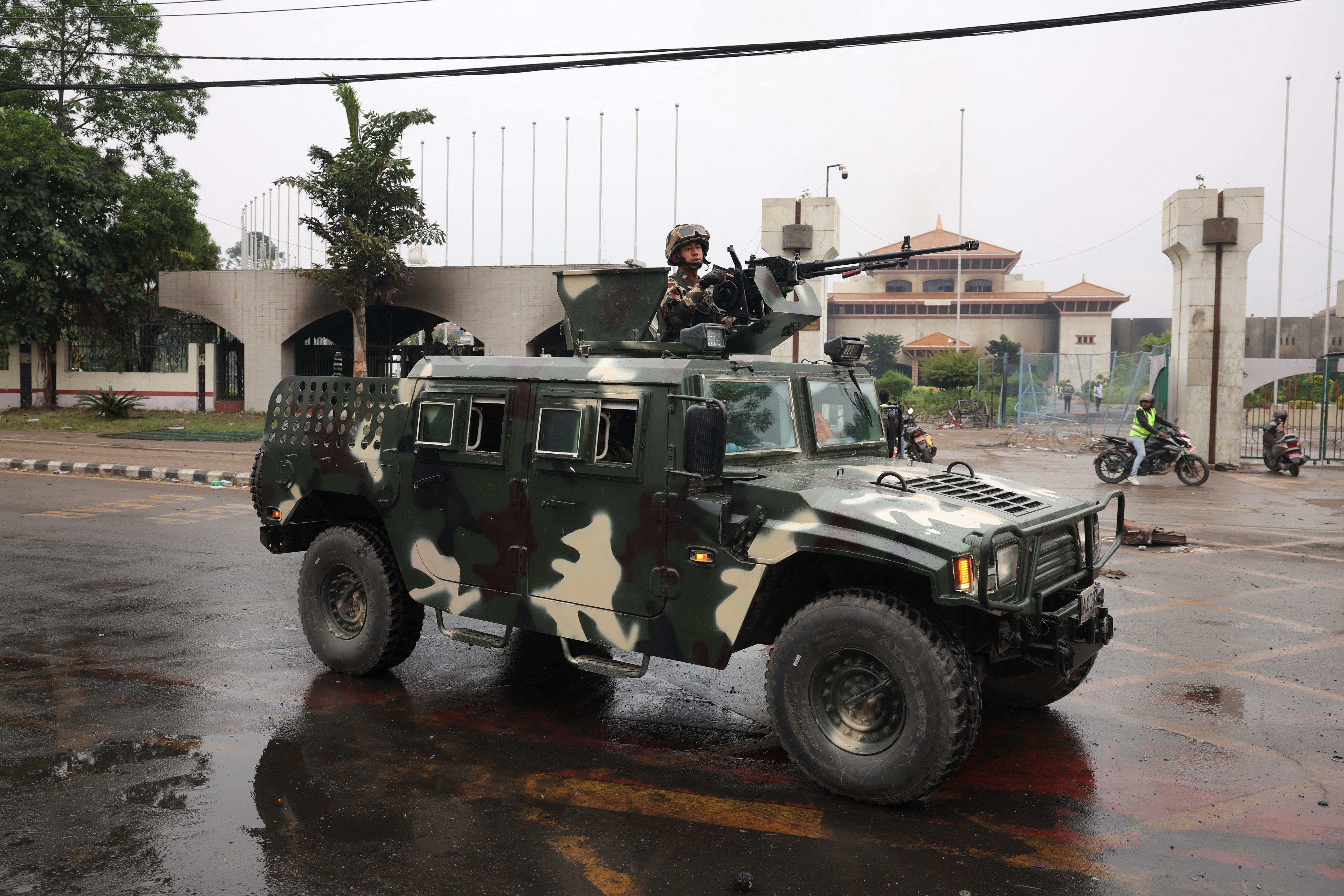 A Nepali Army solider stands in an armoured vehicle driving past the Parliament house which was set on fire by protesters