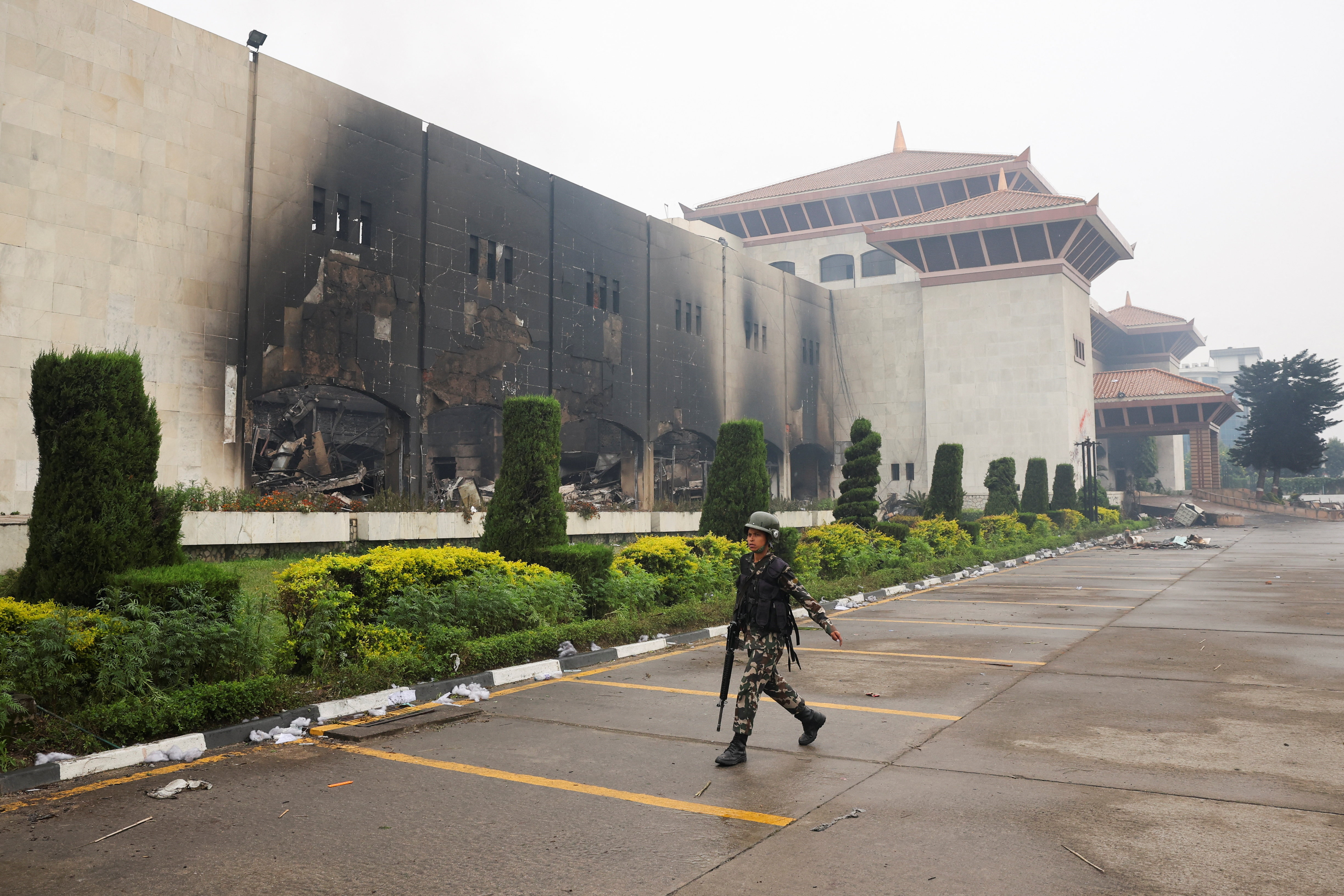 A Nepali army soldier walks in front of the Parliament house which was set on fire by the protesters, following Monday's killing of 19 people after anti-corruption protests