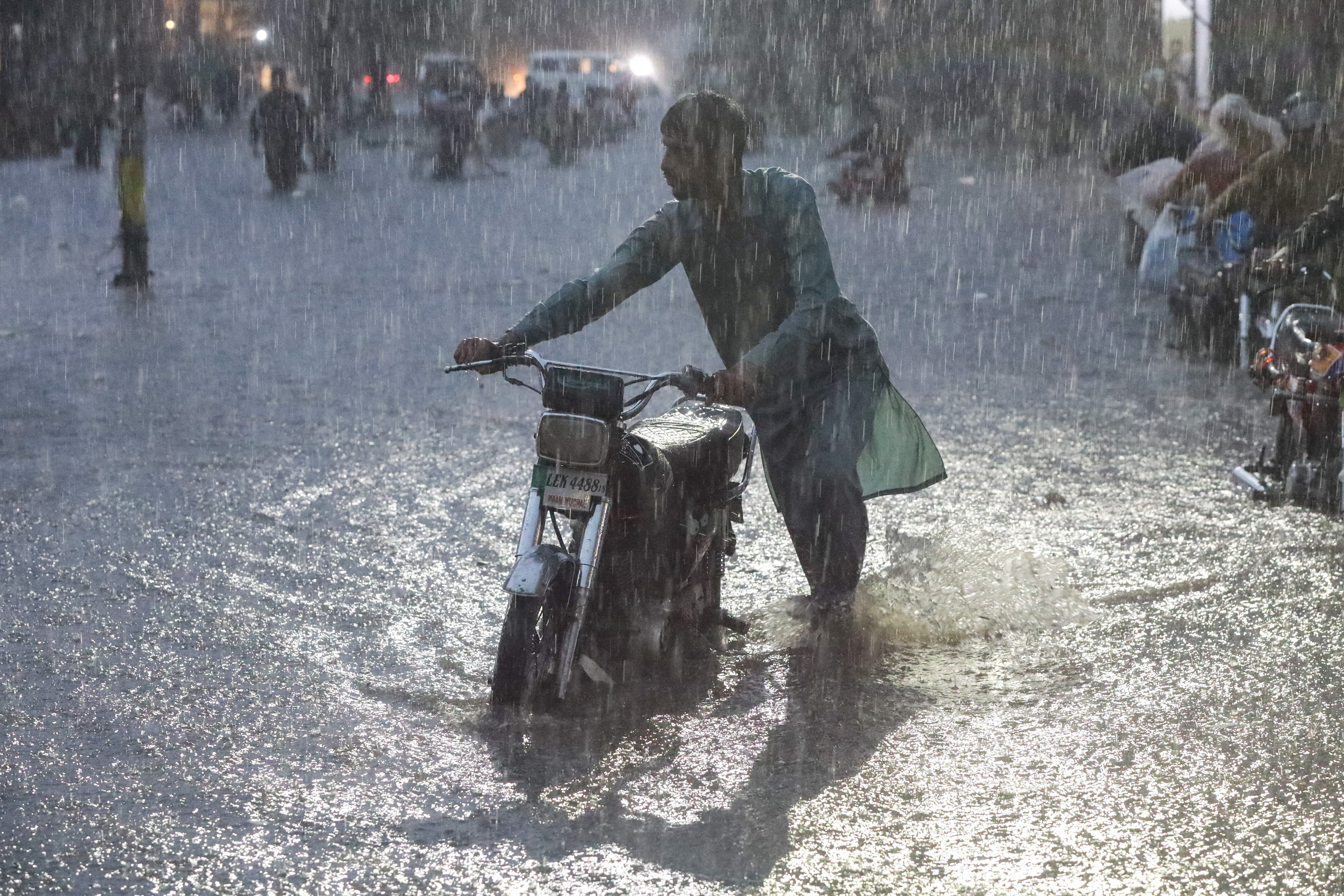 A man pushes his motorbike as he wades through a flooded road amid rain in Lahore, Pakistan