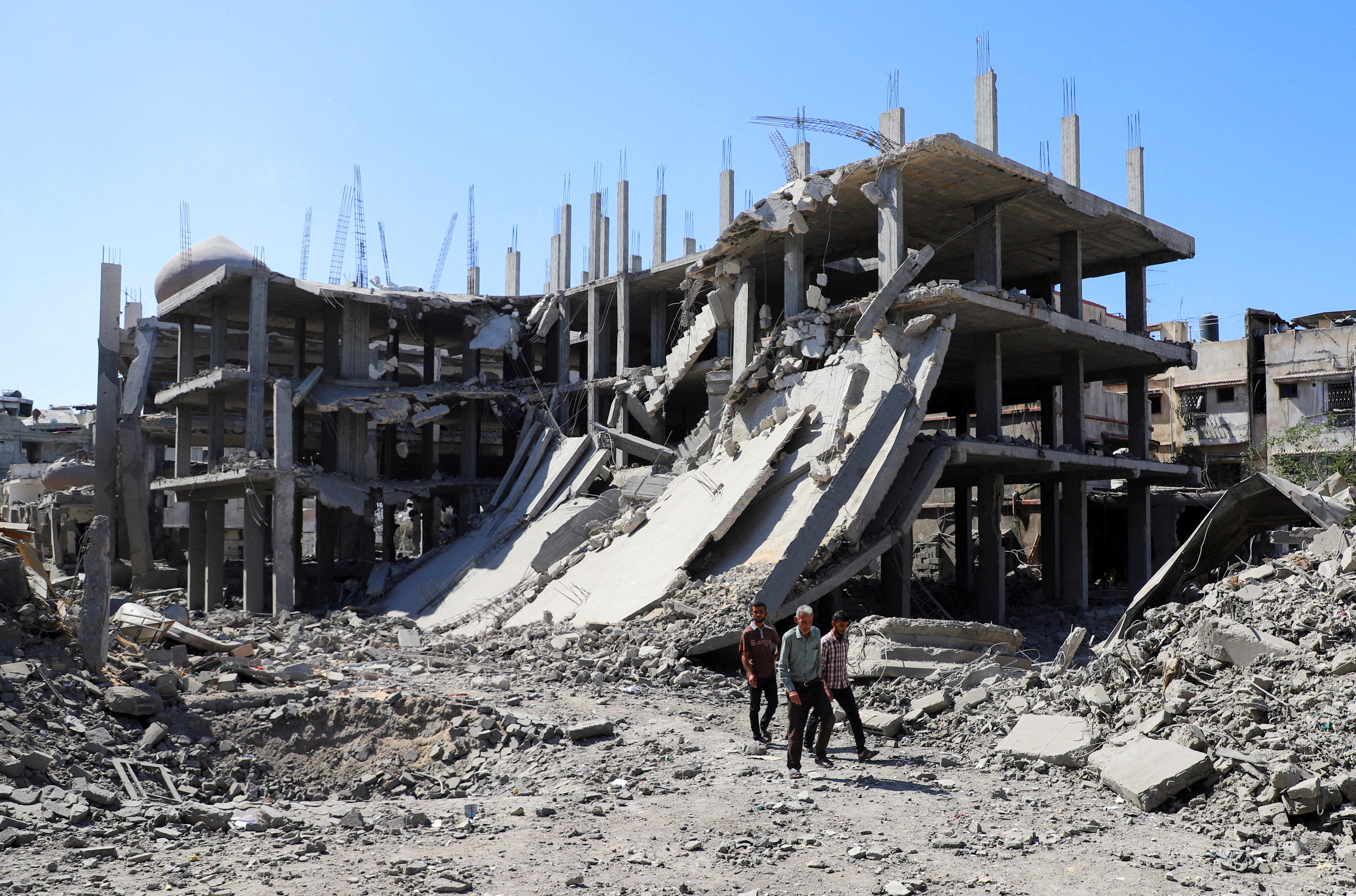 Palestinians walk past a destroyed building, as they inspect the damage in the aftermath of Israeli operation at Sabra neighbourhood in Gaza City, October 8, 2025.