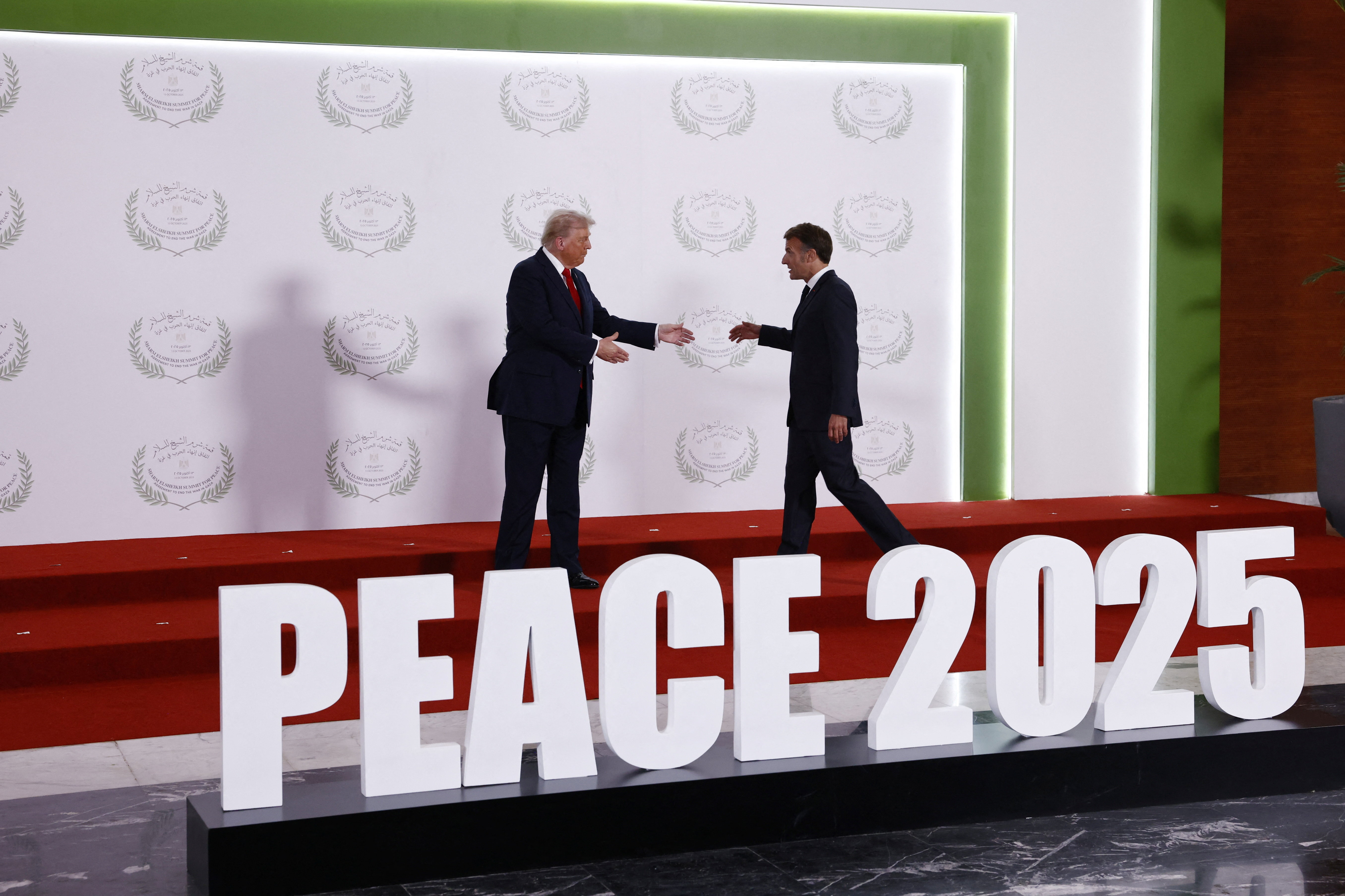 U.S. President Donald Trump greets French President Emmanuel Macron as they prepare to pose for a photo, at a world leaders' summit on ending the Gaza war.