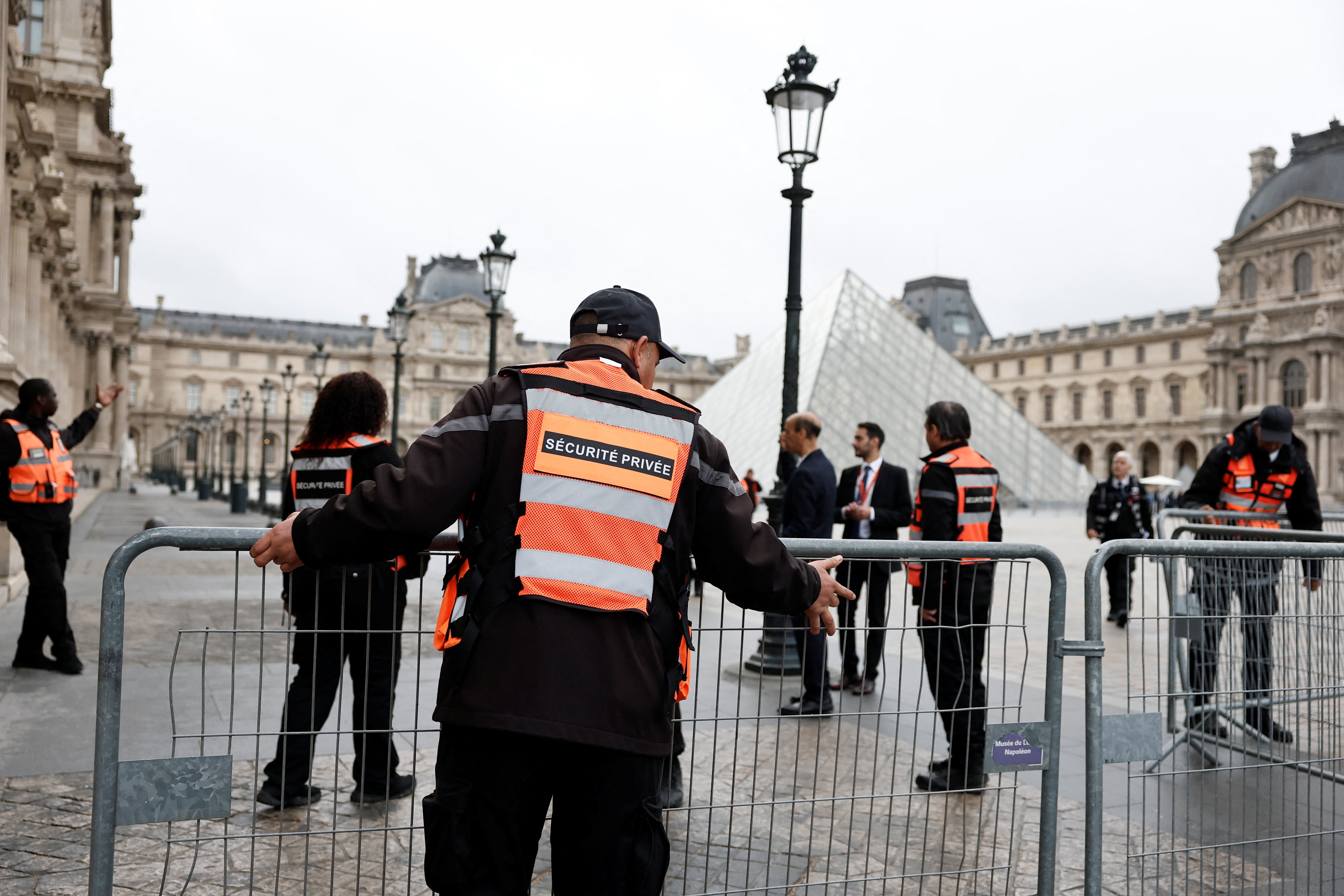 Security employees install barriers near the glass Pyramid of the Louvre Museum as the museum remains closed the day after a spectacular jewel heist by thieves
