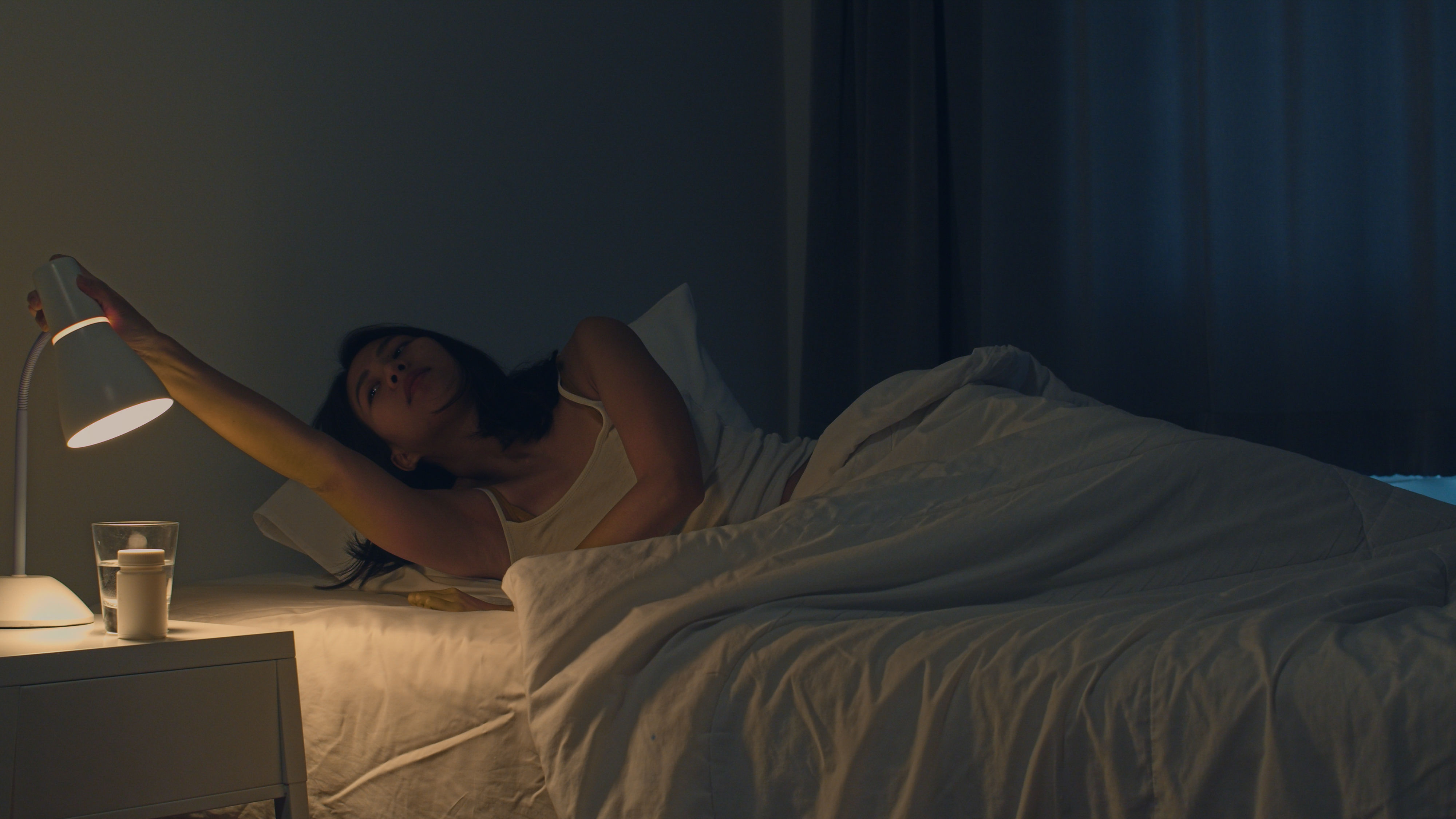 Beautiful Asian young woman sleeping cozily in her bedroom. Indian female hand turning off on light switch near bed in room at home in late night ready to sleep. Sweet dreams and relaxation concept.