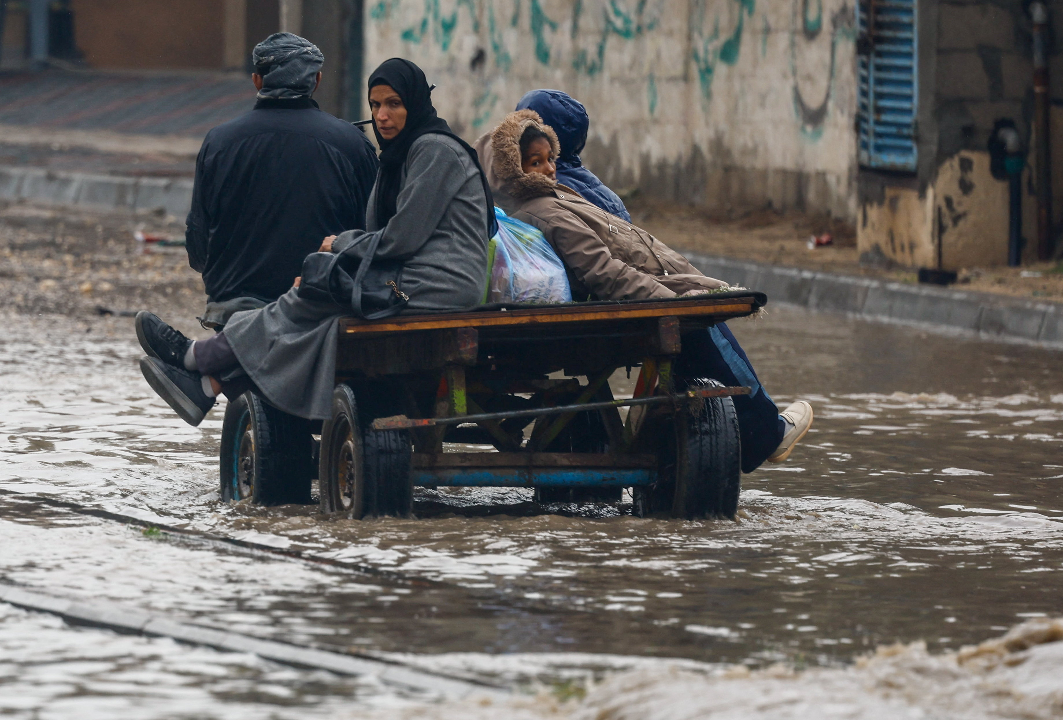 Displaced Palestinians make their way through a flooded street on a cart, during a rainy day in Nuseirat, central Gaza Strip, December 11, 2025. REUTERS/Mahmoud Issa