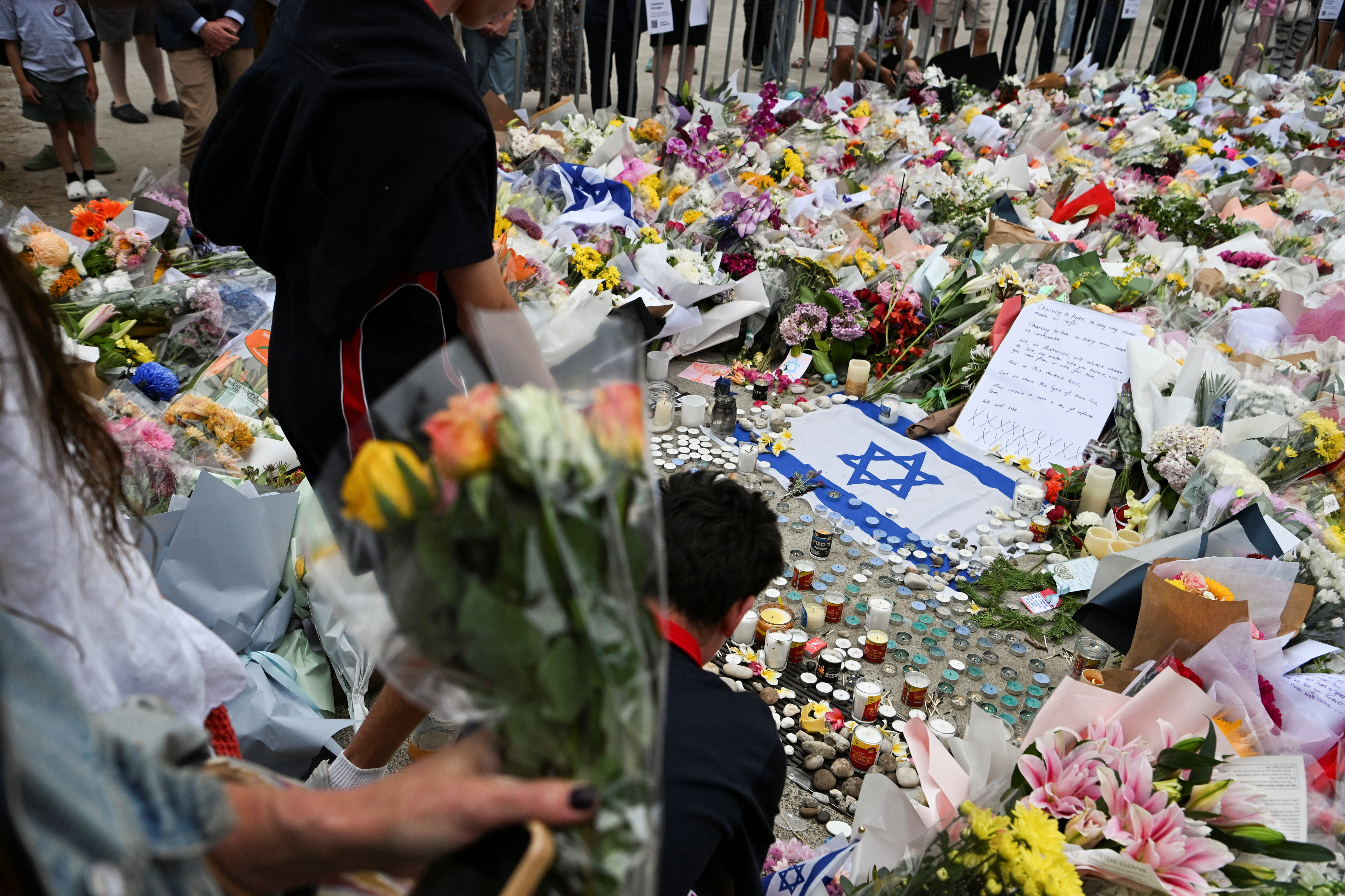 People stand near flowers laid as a tribute at Bondi Beach to honour the victims of a mass shooting that targeted a Hanukkah celebration at Bondi Beach on Sunday, in Sydney, Australia, December 16, 2025. REUTERS/Flavio Brancaleone
