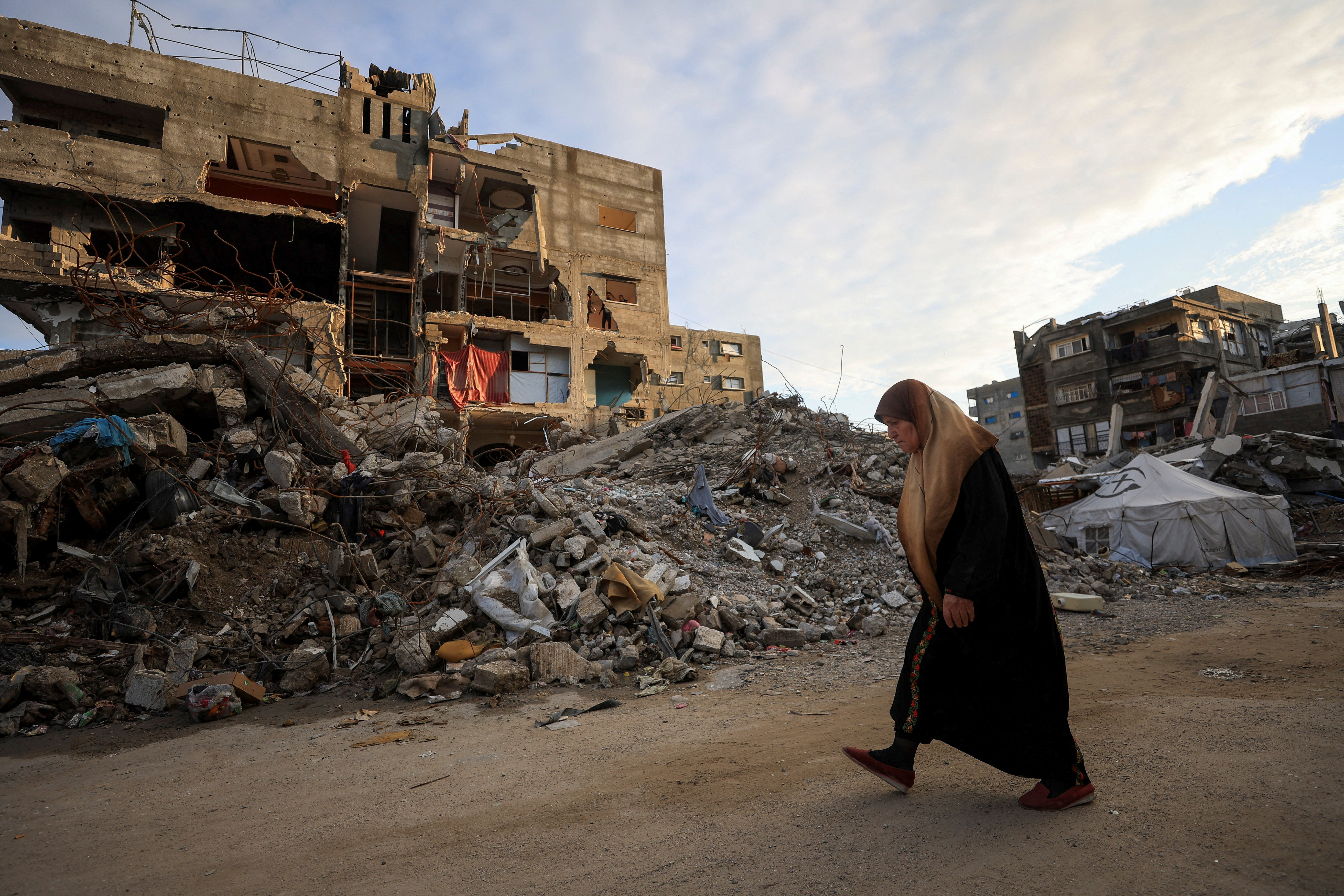 FILE PHOTO: A Palestinian woman walks past residential buildings damaged and destroyed during the war, in Gaza City, December 14, 2025.