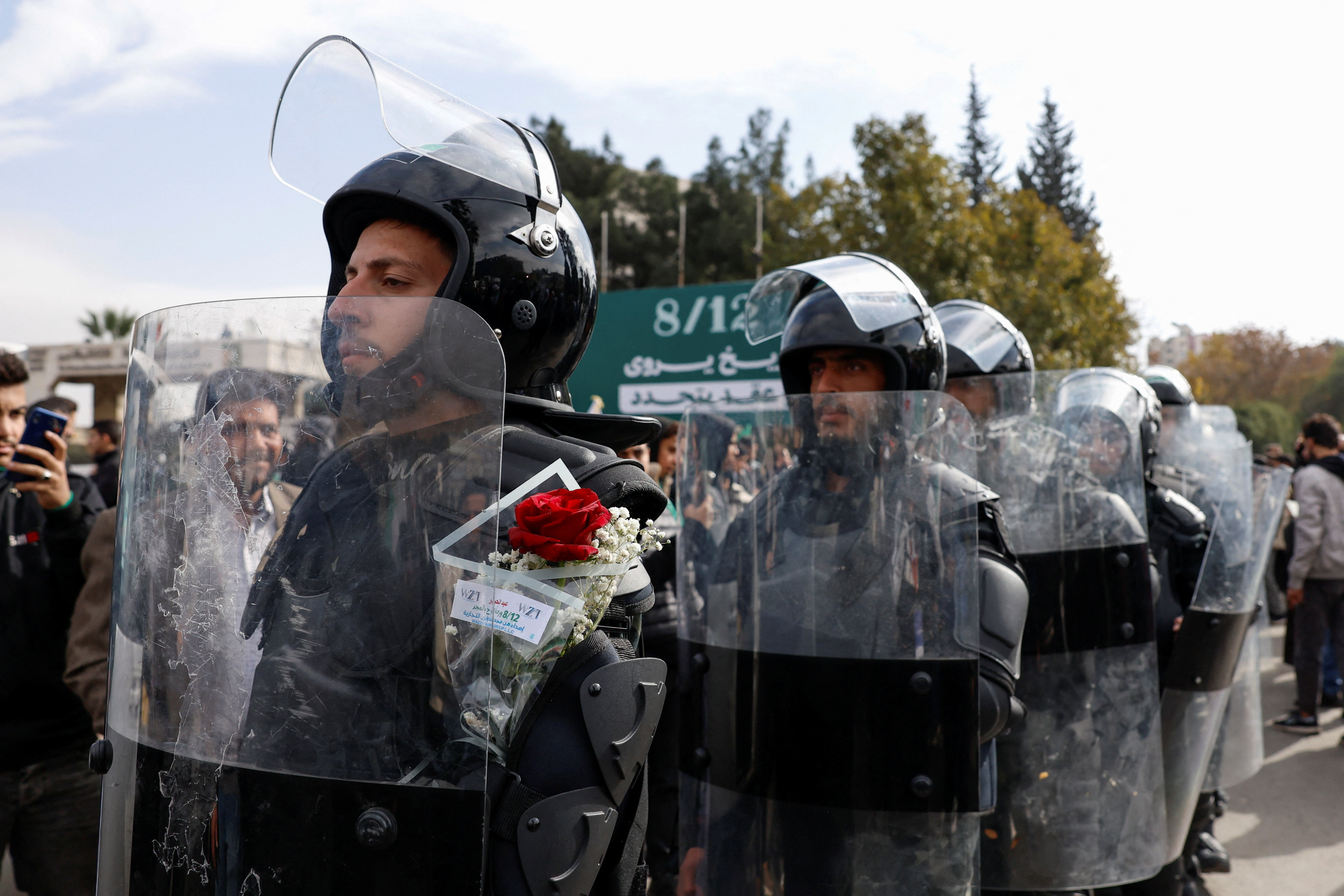 A Syrian police officer carries flowers behind his shield during the celebration of the first anniversary of Bashar al-Assad's fall, at Ummayad Square in Damascus, Syria, December 8, 2025.