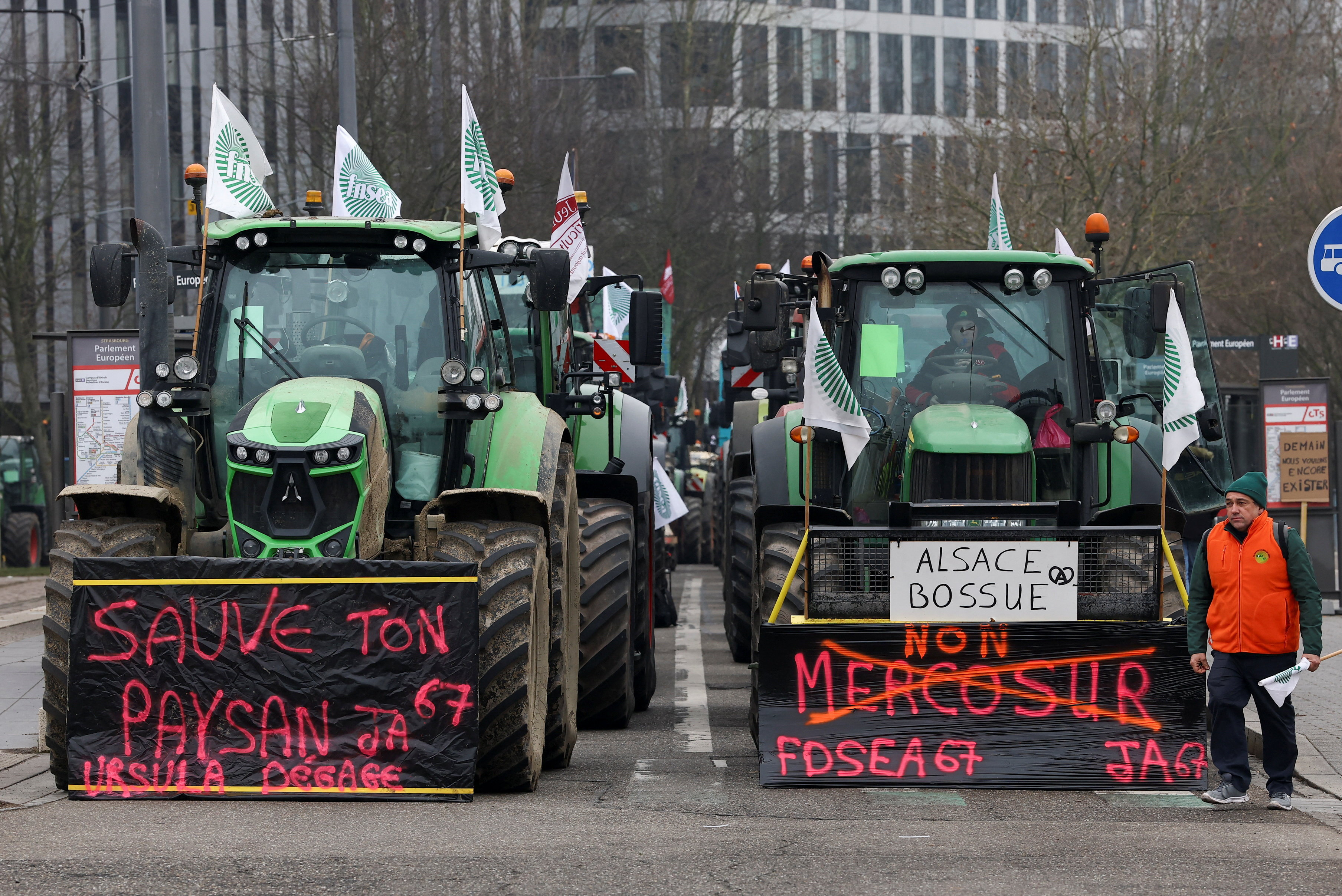 French farmers from FNSEA and Jeunes Agriculteurs farm unions sit in their tractors with messages reading "Save your farmers. Ursula go away." and " No Mercosur" along a road near the European Parliament