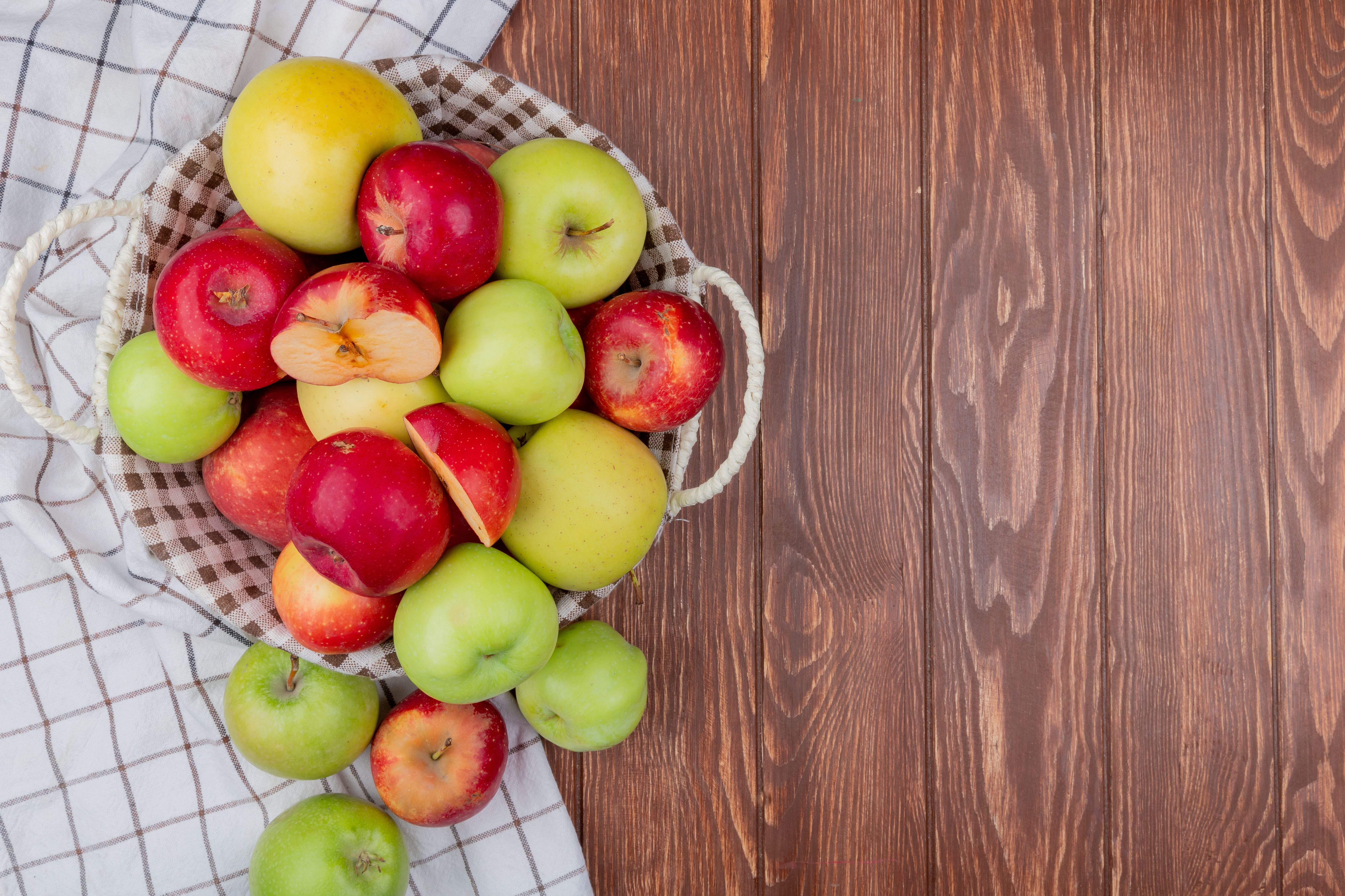 top view of cut and whole apples in basket and on plaid cloth on wooden background with copy space