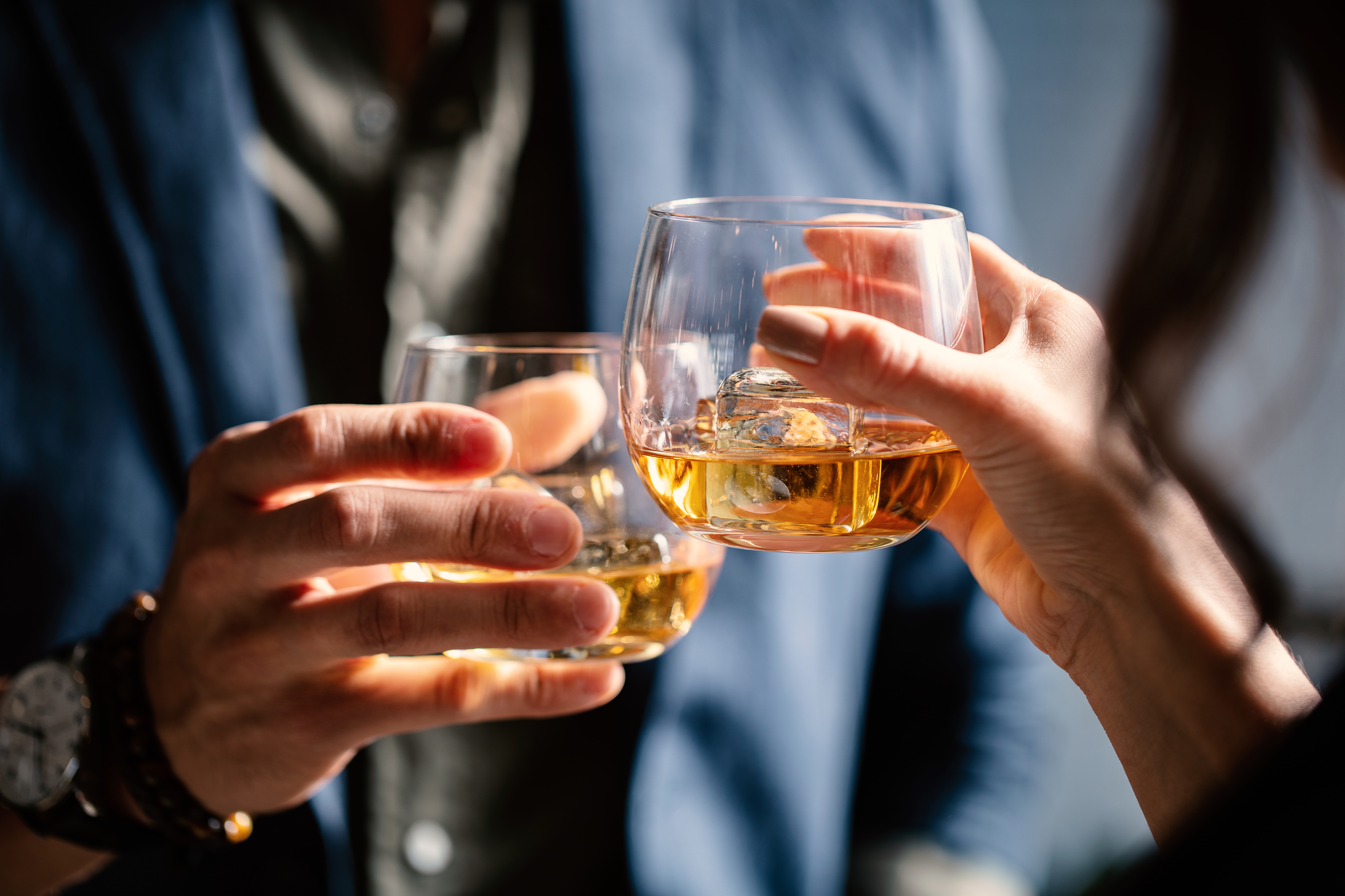 A closeup shot of two people clinking glasses with alcohol at a toast
