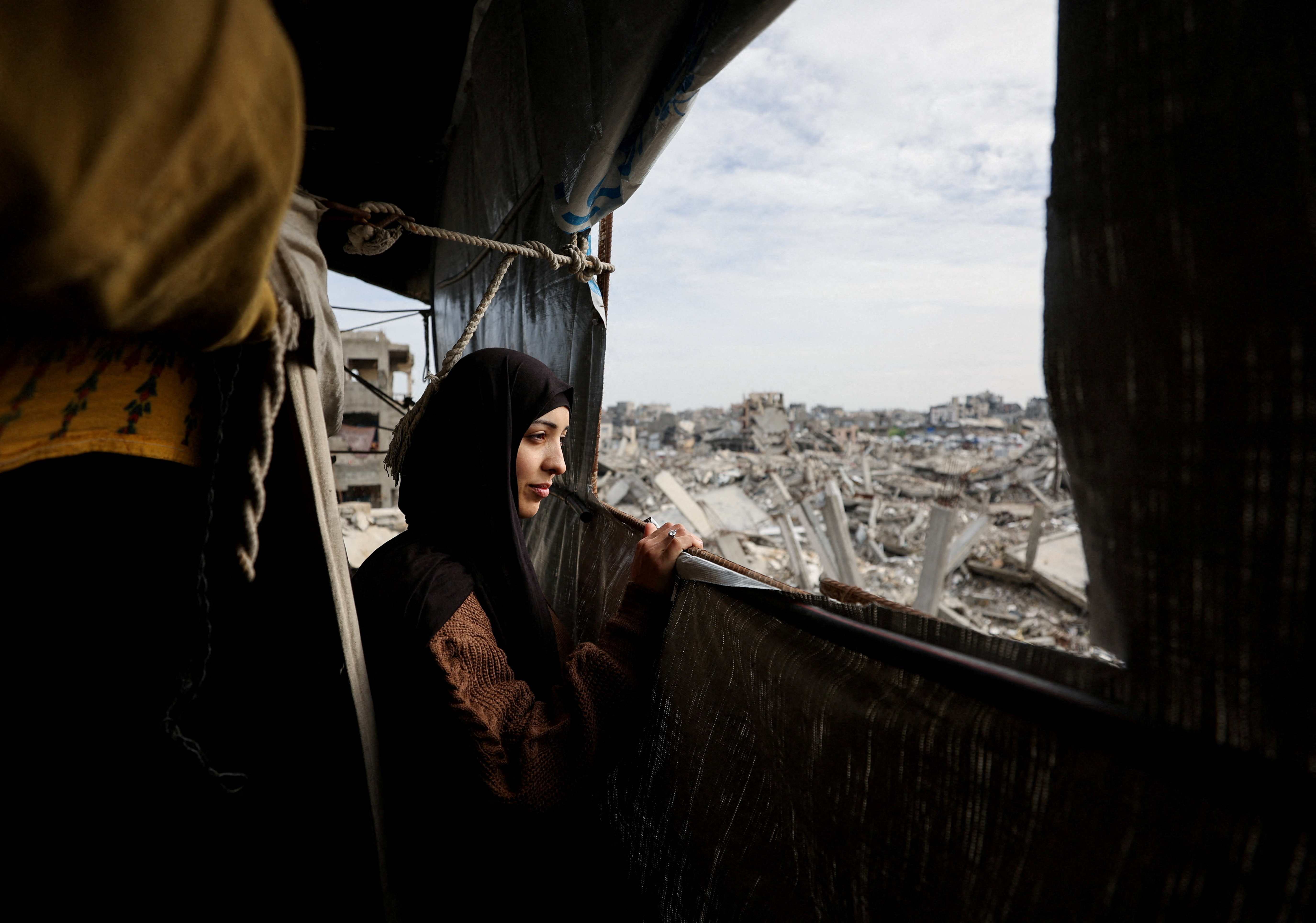Palestinian mother of three, Eatedal Rayyan, 29, sits and looks out from a window of a tent set up inside her war-damaged home, following her return from medical treatment in Egypt