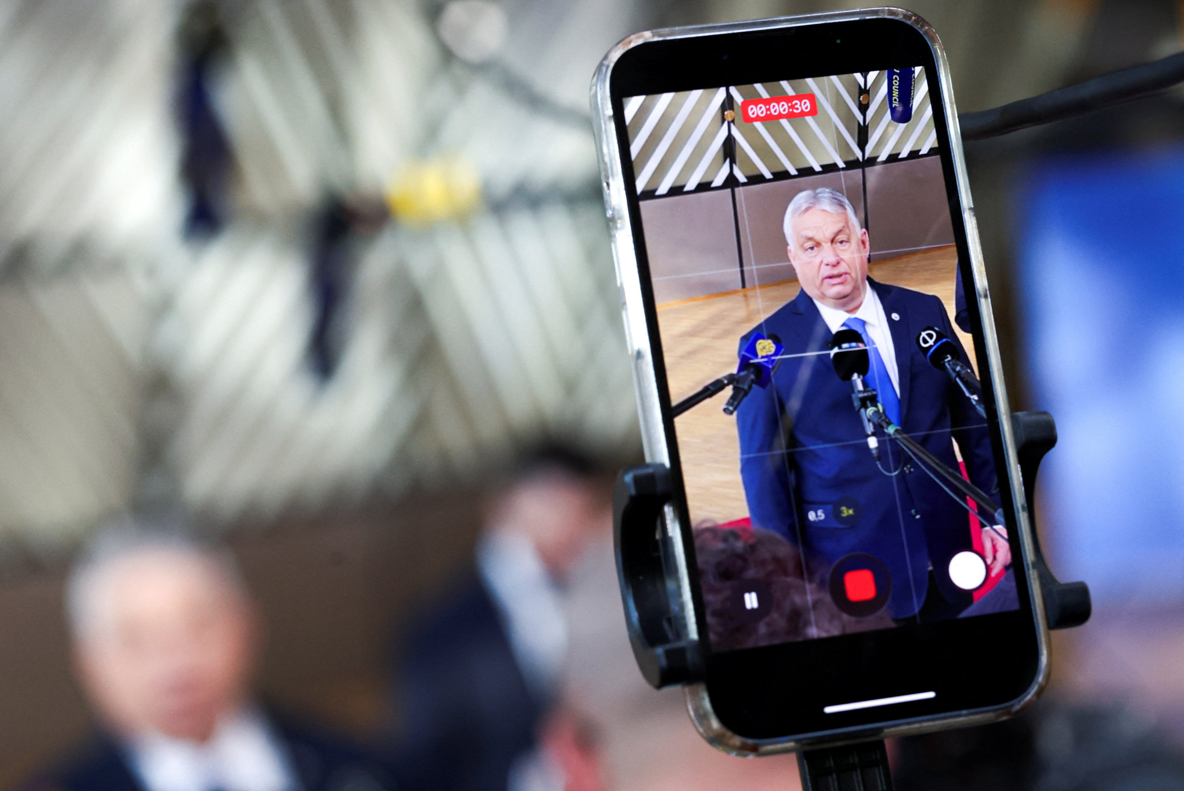 A smartphone records Hungarian Prime Minister Viktor Orban speaking to the press upon his arrival for a European Union leaders' summit in Brussels, Belgium, March 19, 2026. REUTERS/Yves Herman