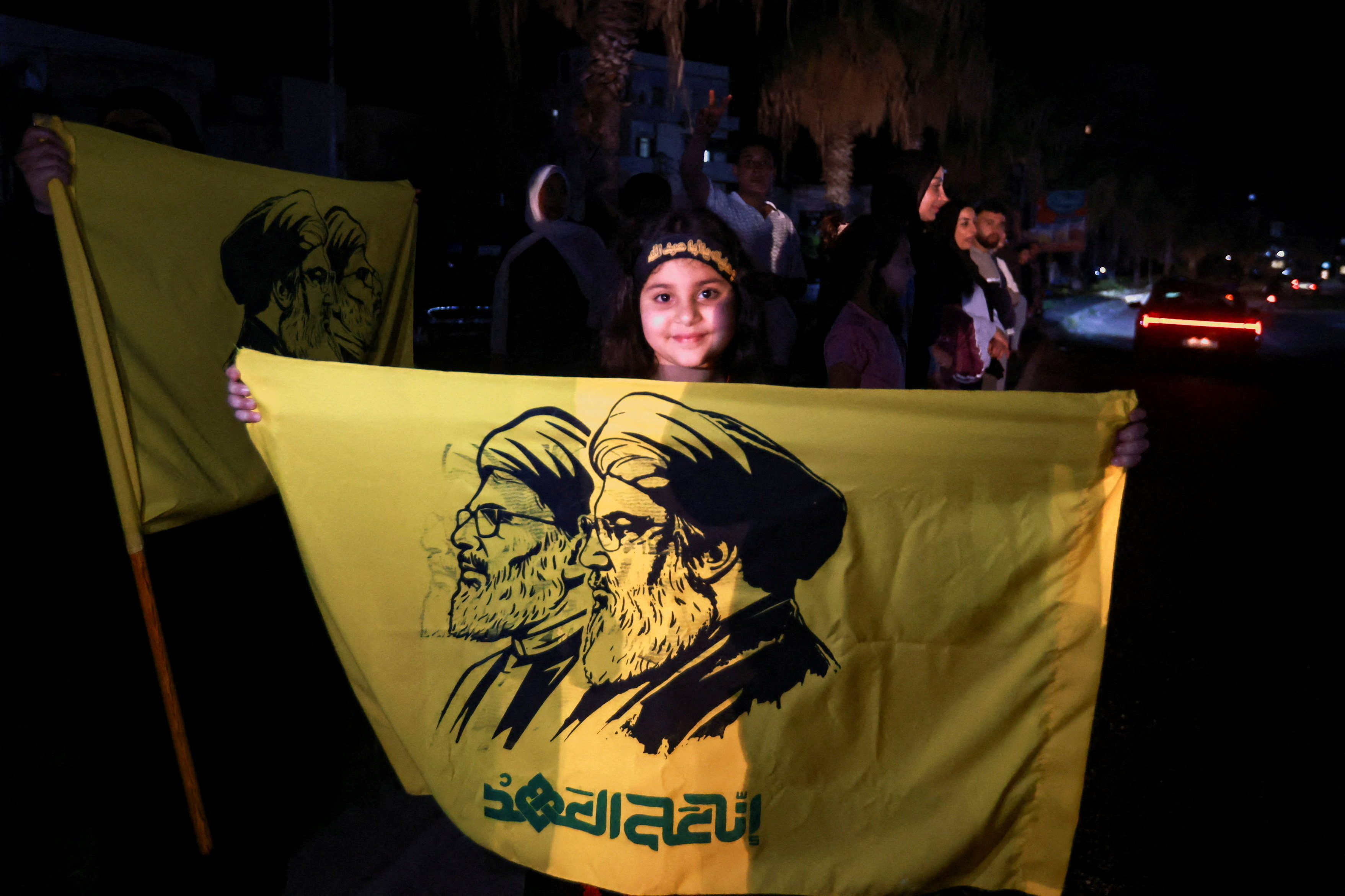 A girl holds a flag with an image depicting former Hezbollah leaders Hassan Nasrallah and Hashem Safieddine, as displaced people return to their homes after a 10-day ceasefire between Lebanon and Israel went into effect