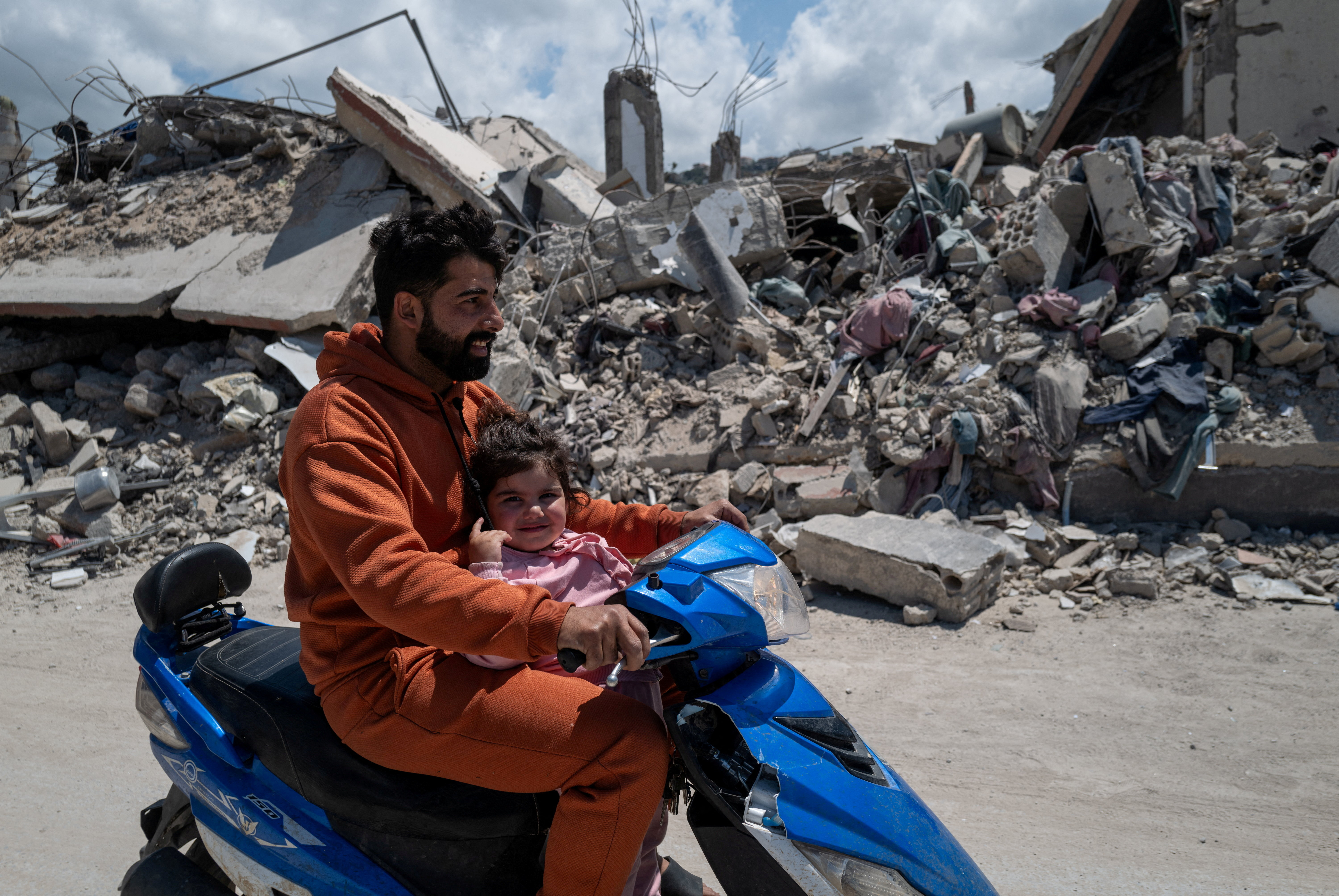 Mhamed, 34, and Taline 2,5 years old, ride  a motorcycle past buildings damaged by an Israeli strike in Mansouri village, southern Lebanon, amid a 10-day ceasefire between Lebanon and Israel, April 21, 2026.