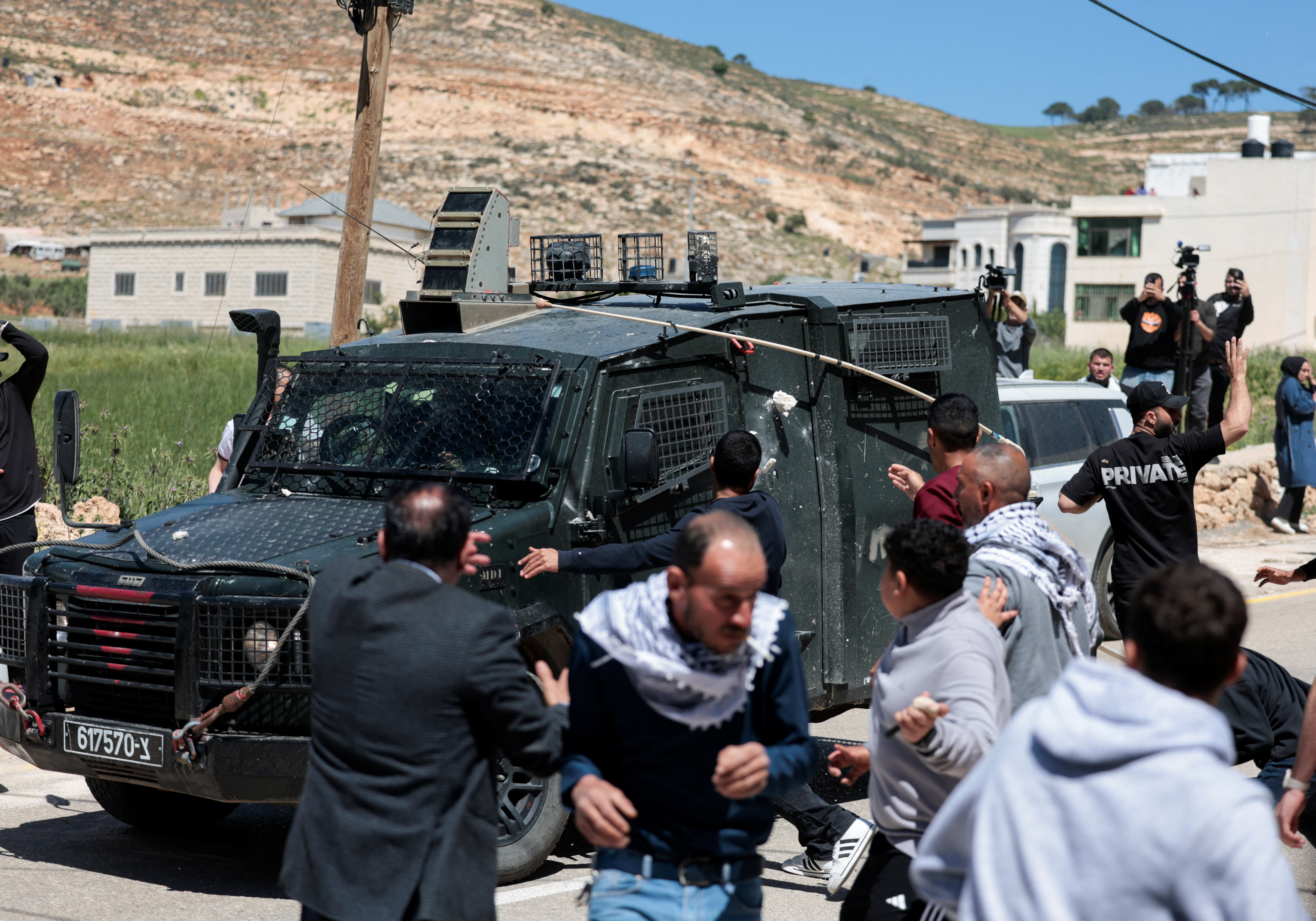 Mourners hurl stones at an Israeli military vehicle amid clashes during the funeral for two Palestinians killed after Israeli settlers and soldiers opened fire, according to witnesses
