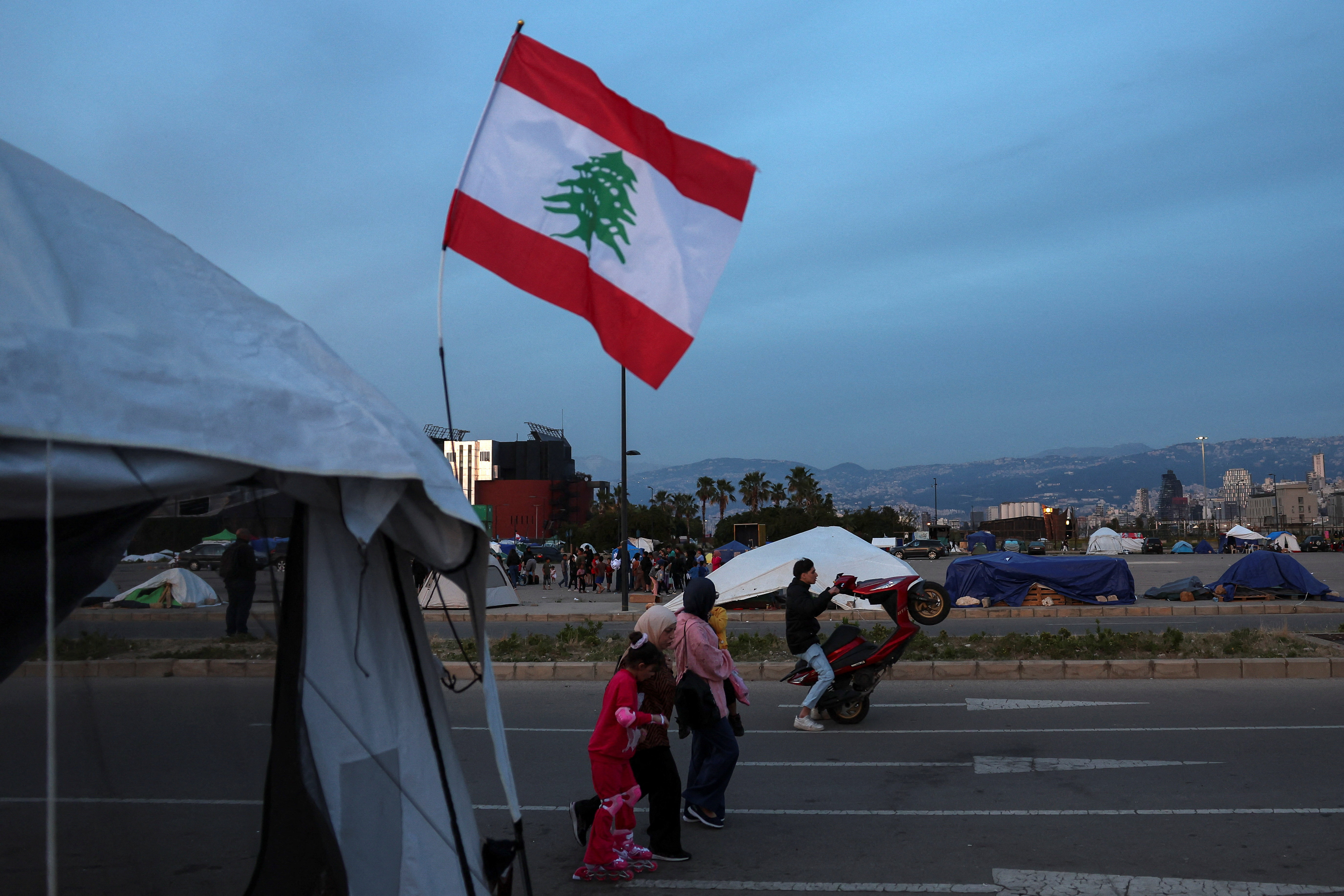 A man rides a motorcycle as displaced people walk at a makeshift encampment amid a temporary ceasefire between Lebanon and Israel, in Beirut, Lebanon, April 24, 2026.