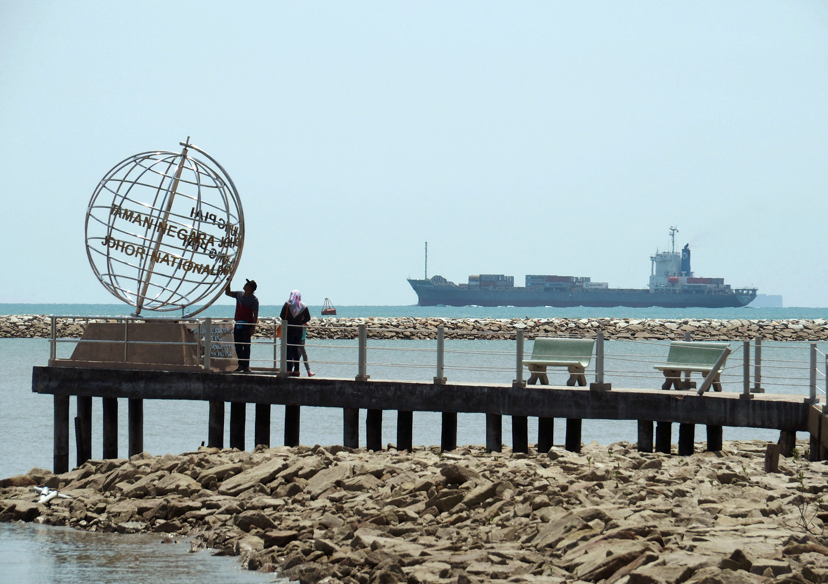 FILE PHOTO: A container ship enters the Singapore Strait for the Strait of Malacca, as tourists stand at mainland Asia's southern most point in Johor, Malaysia November 12, 2016.