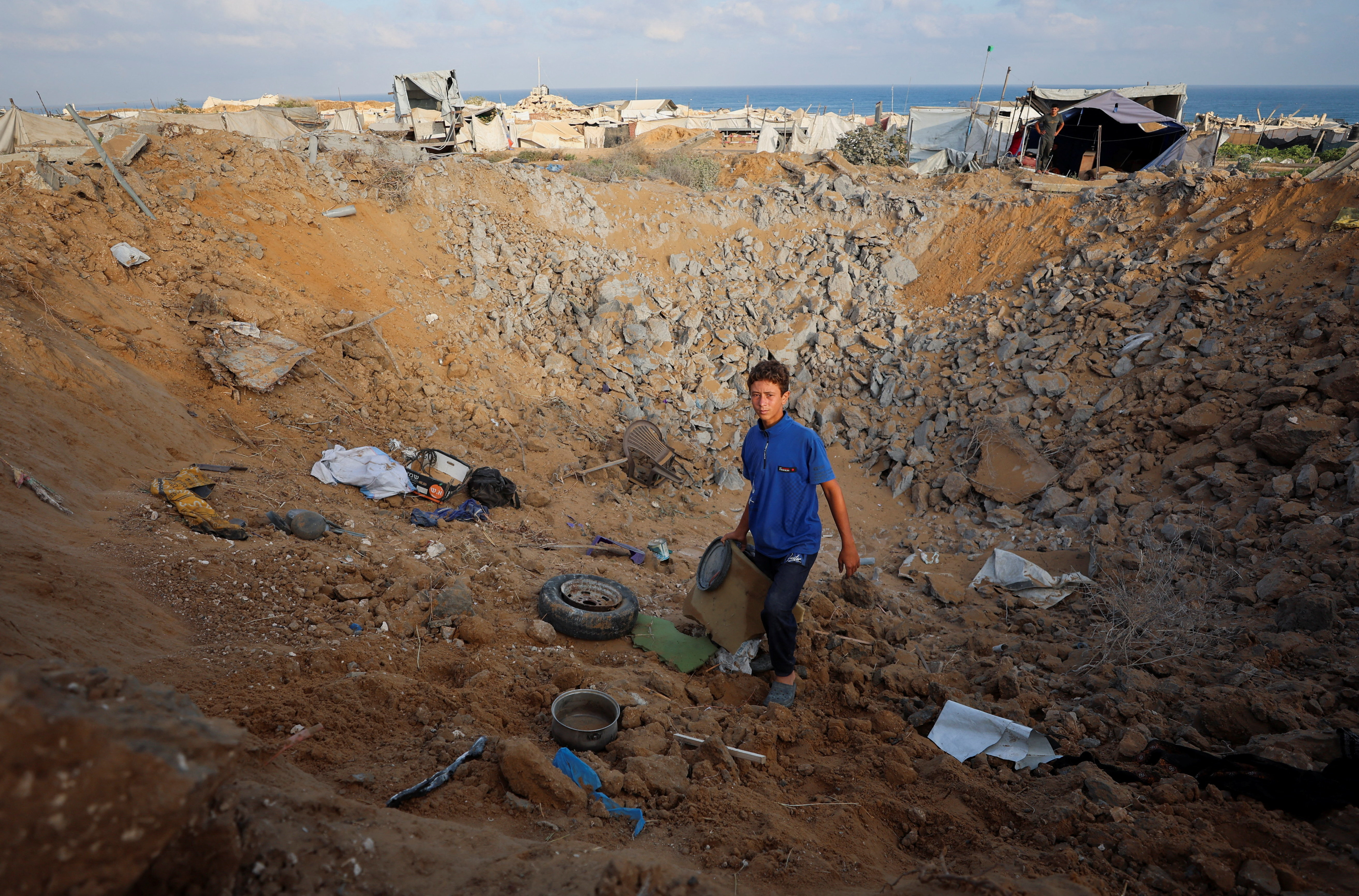 A boy looks on as Palestinians inspect the site of an Israeli strike on a tent camp sheltering displaced people, who were warned to evacuate before the attack, in Gaza City, June 24, 2026.
