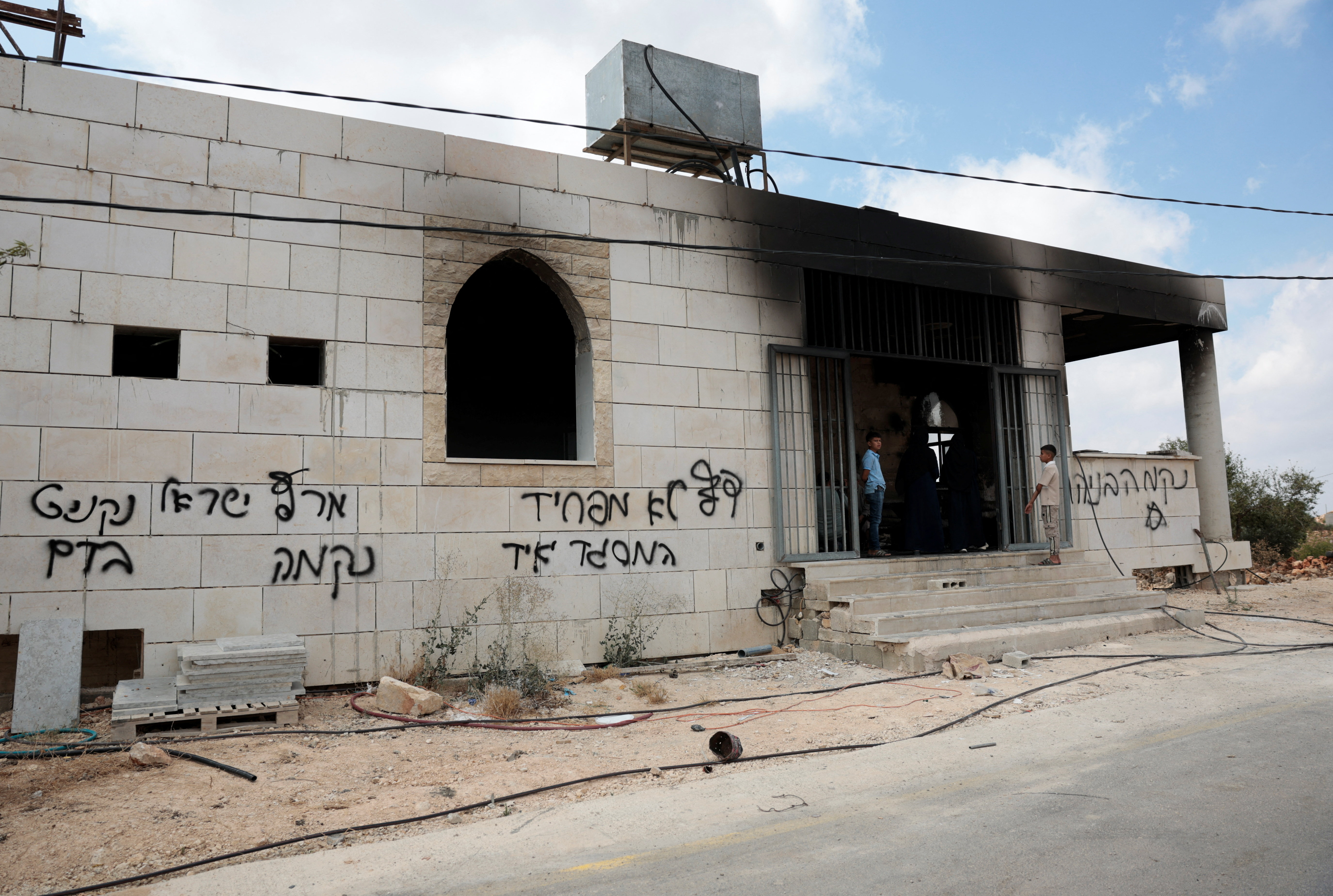 Palestinian boys stand at a damaged a mosque, which Palestinians say was damaged by Israeli settlers, in Qusra near Nablus