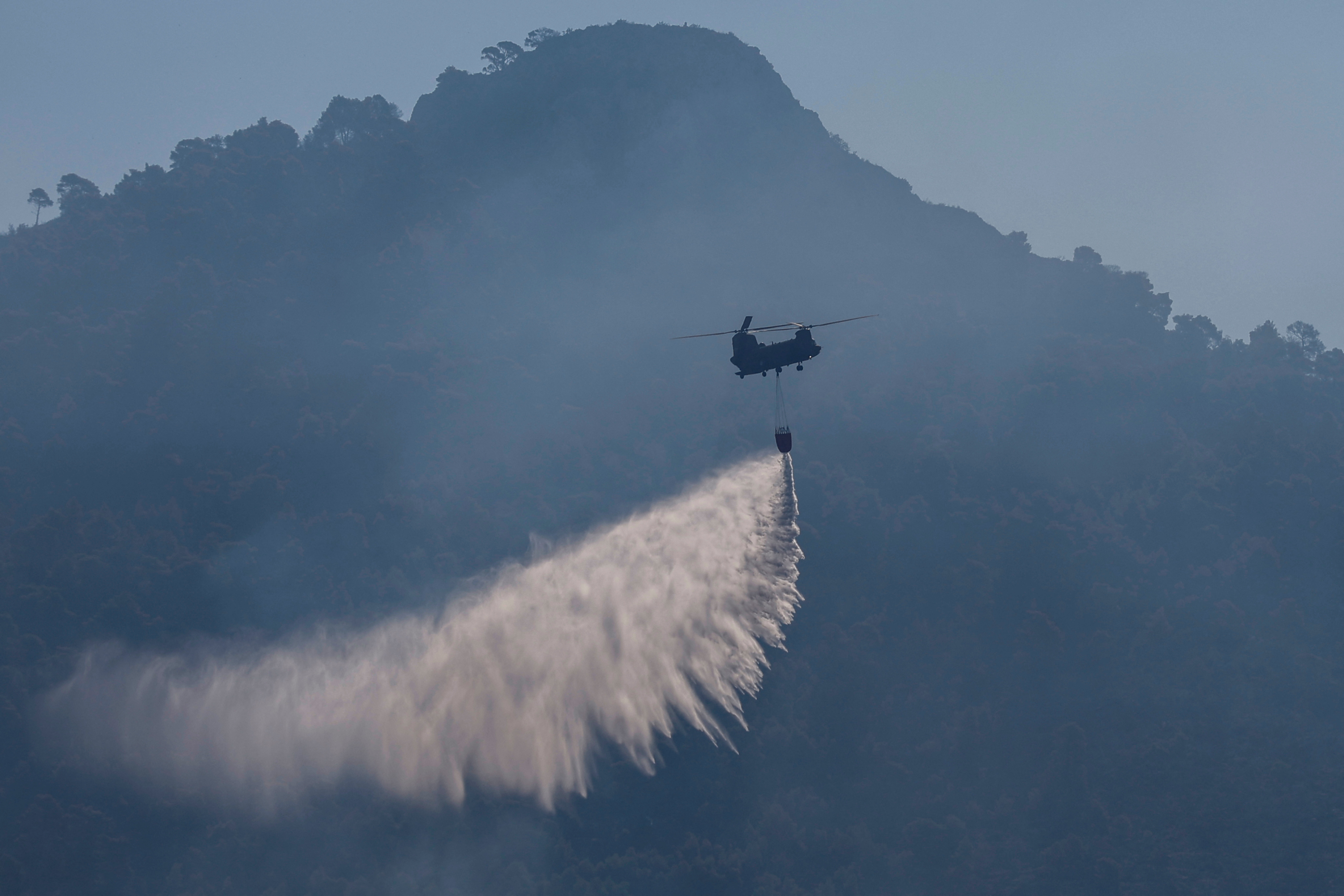 A Chinook helicopter drops water to extinguish fire hotspots in the Kitheronas mountain above Psatha, Greece, August 4, 2026. REUTERS/Louisa Gouliamaki