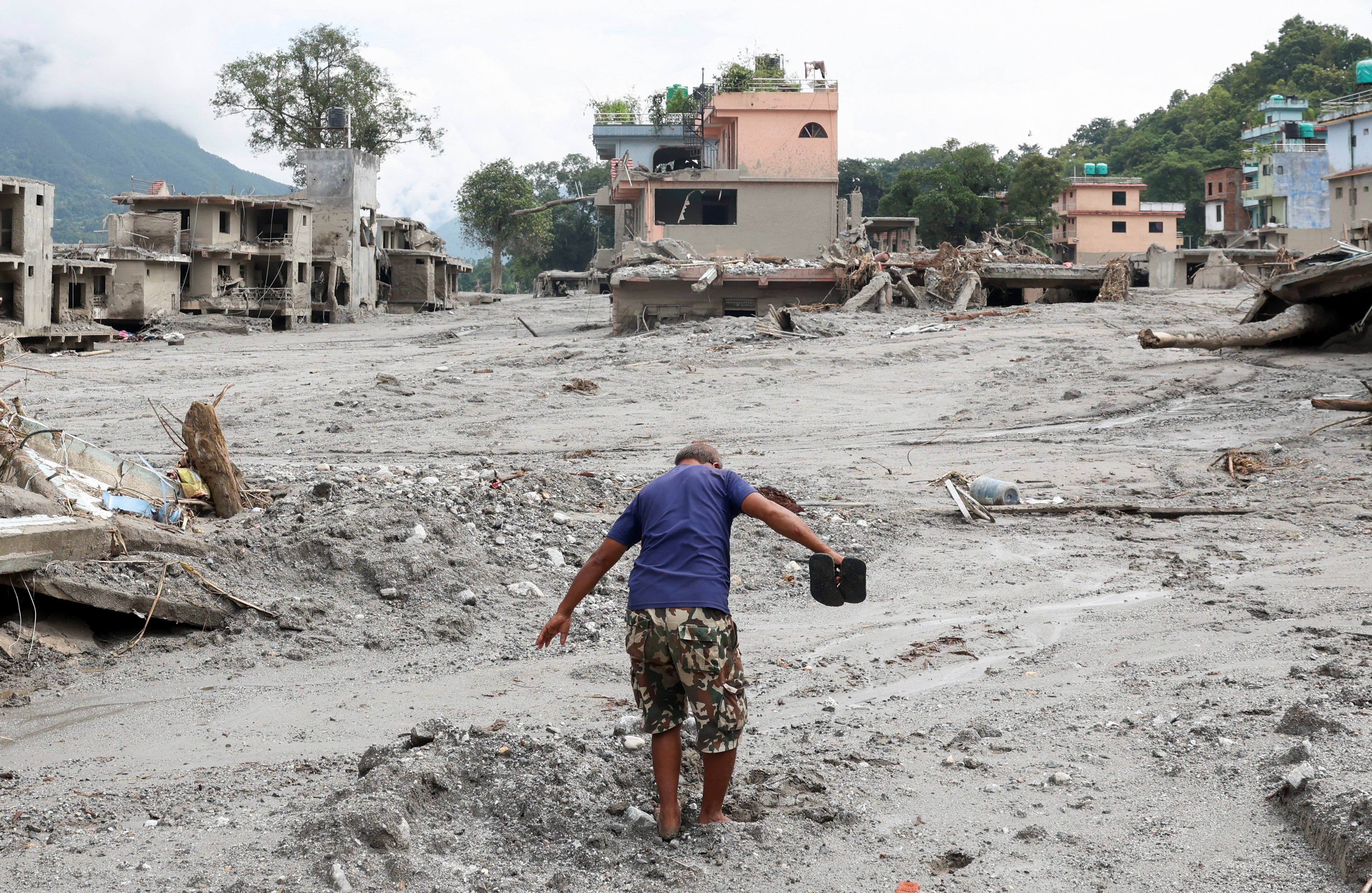 A man navigates through a mud-covered street next to damaged houses following the flash floods and mudslide, at Devighat, Nuwakot district, Nepal, August 29, 2026.