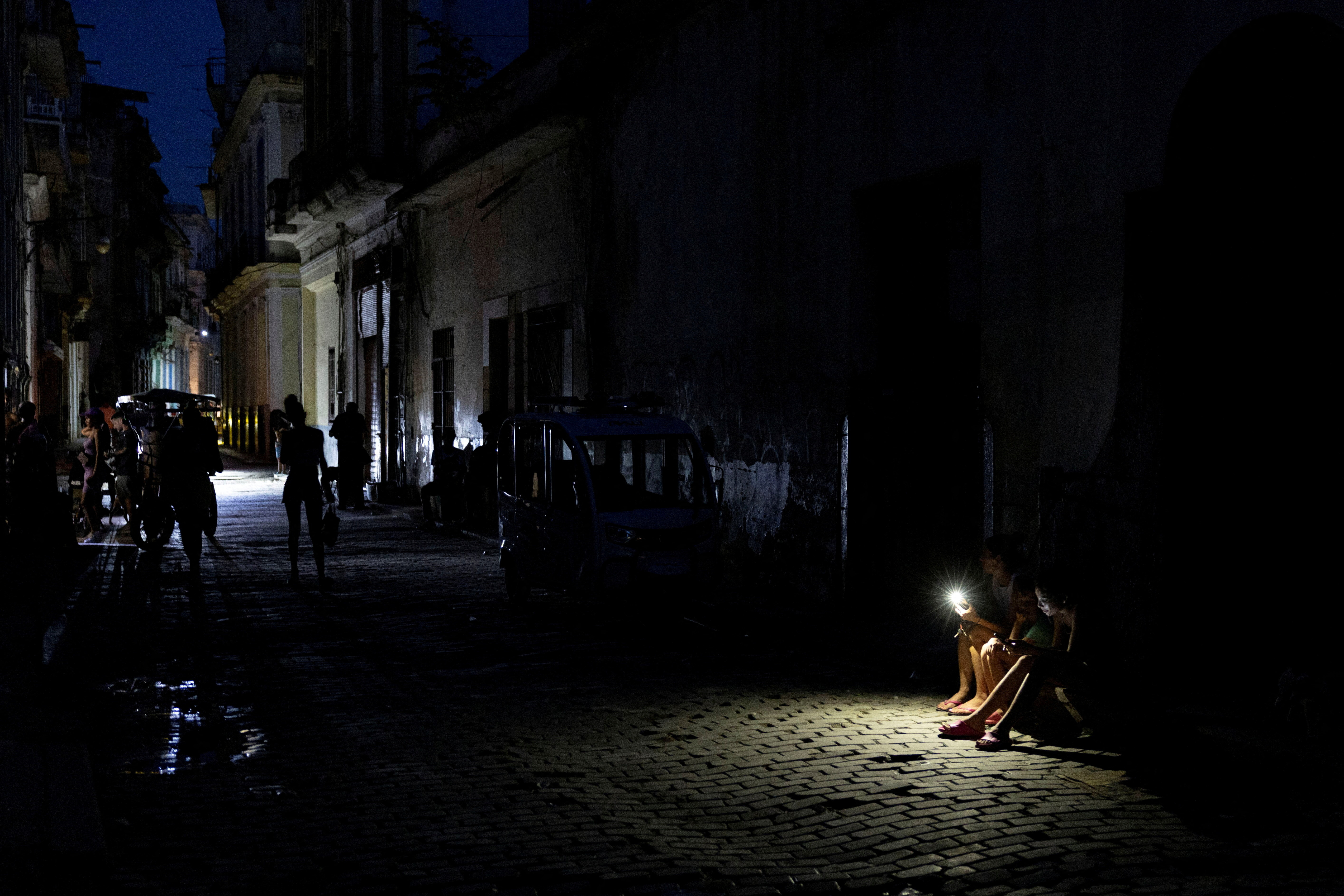People sit on a darkened street illuminated by a mobile phone flashlight during a power outage in Havana, Cuba, September 16, 2026. REUTERS/Ricardo Arduengo     TPX IMAGES OF THE DAY