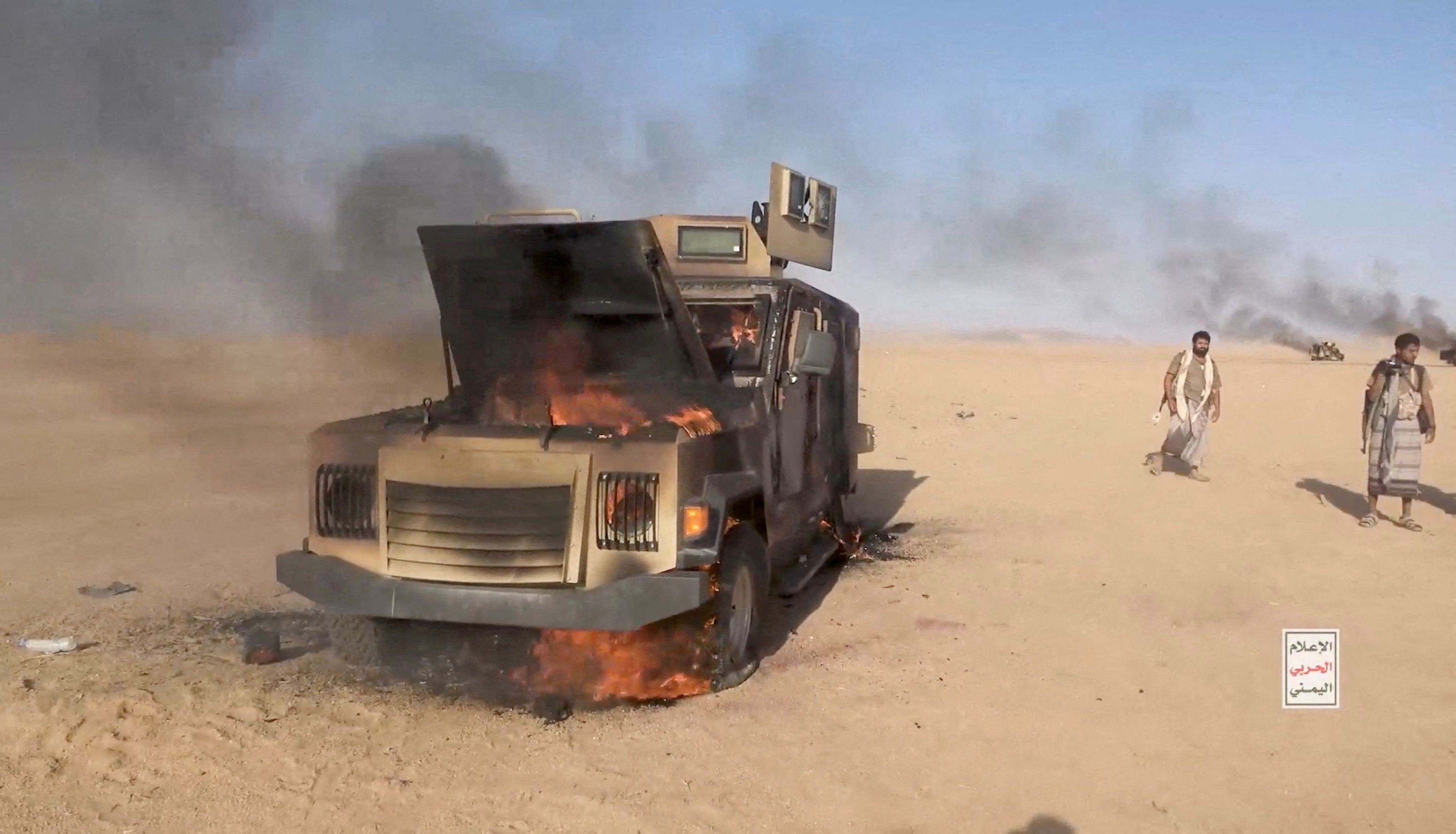 Houthi fighters move next to a destroyed vehicle following what the source described as an attack on Saudi-backed forces in the location given by the source as al Jawf governorate, Yemen