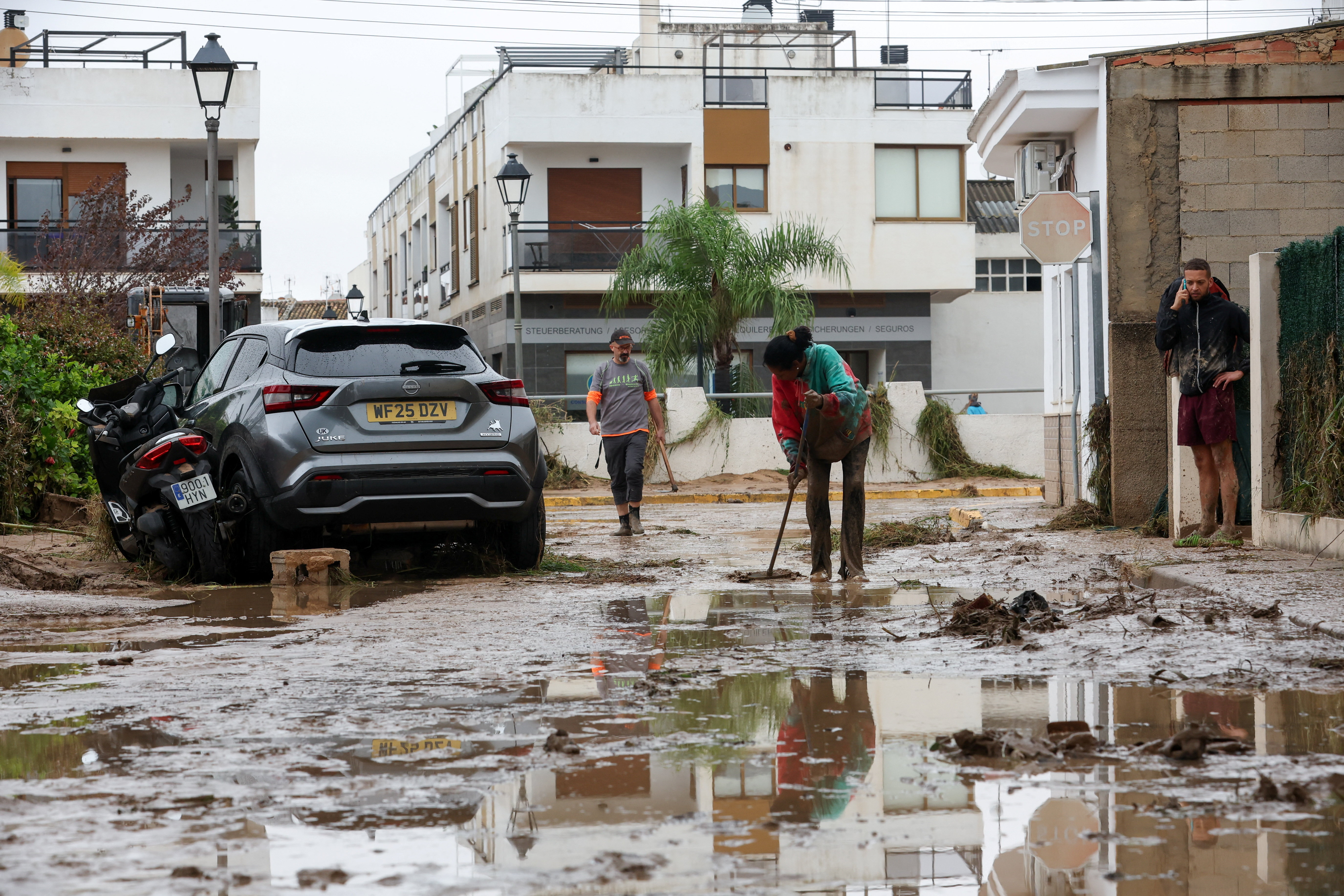 A woman works to clear mud off a road, following torrential rains, which caused floods in eastern Spain, in Els Poblets, Spain, October 19, 2026. REUTERS/Eva Manez