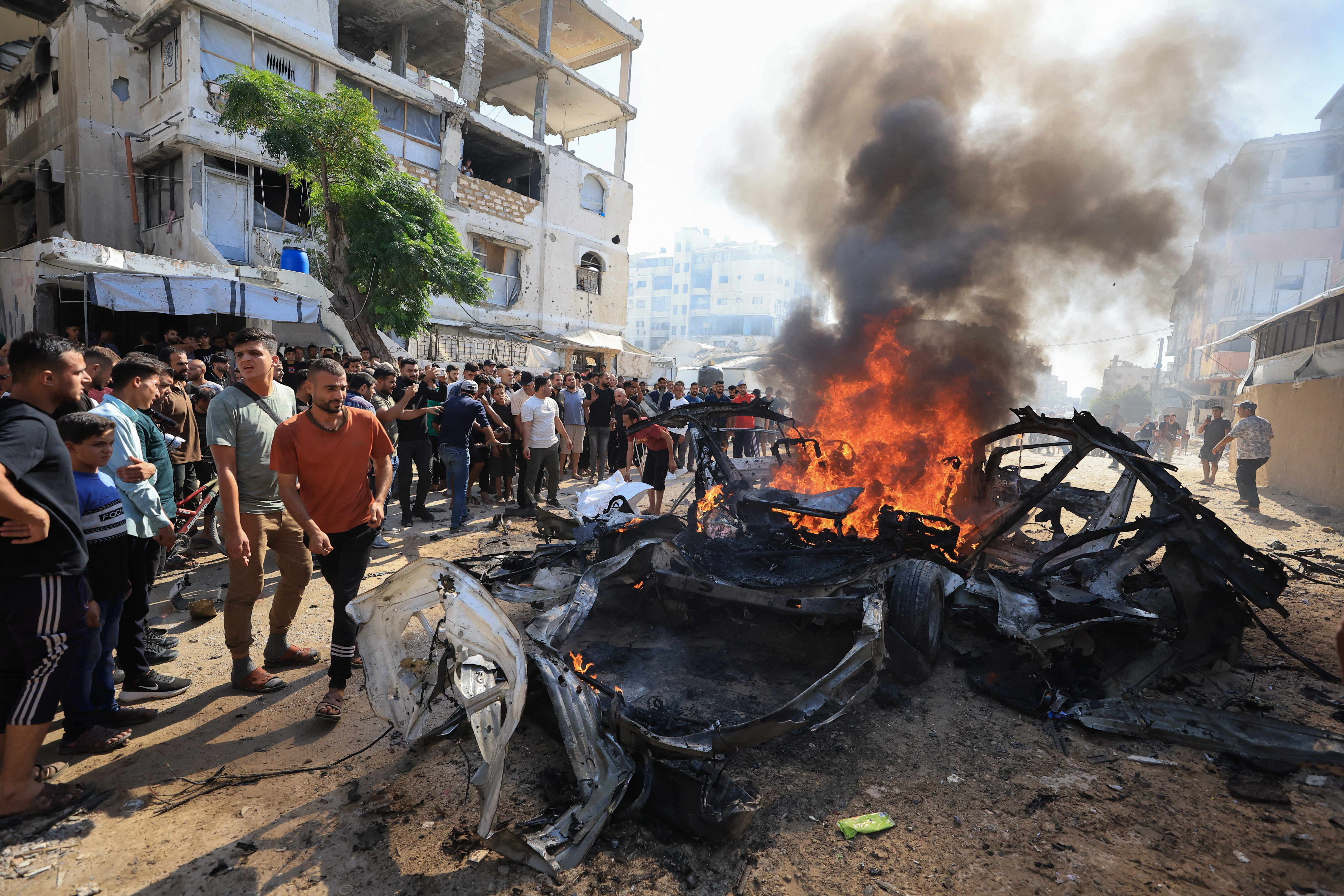 Palestinians gather around a burning a vehicle after it was hit by an Israeli strike, according to health officials, in Gaza City, October 22, 2026.