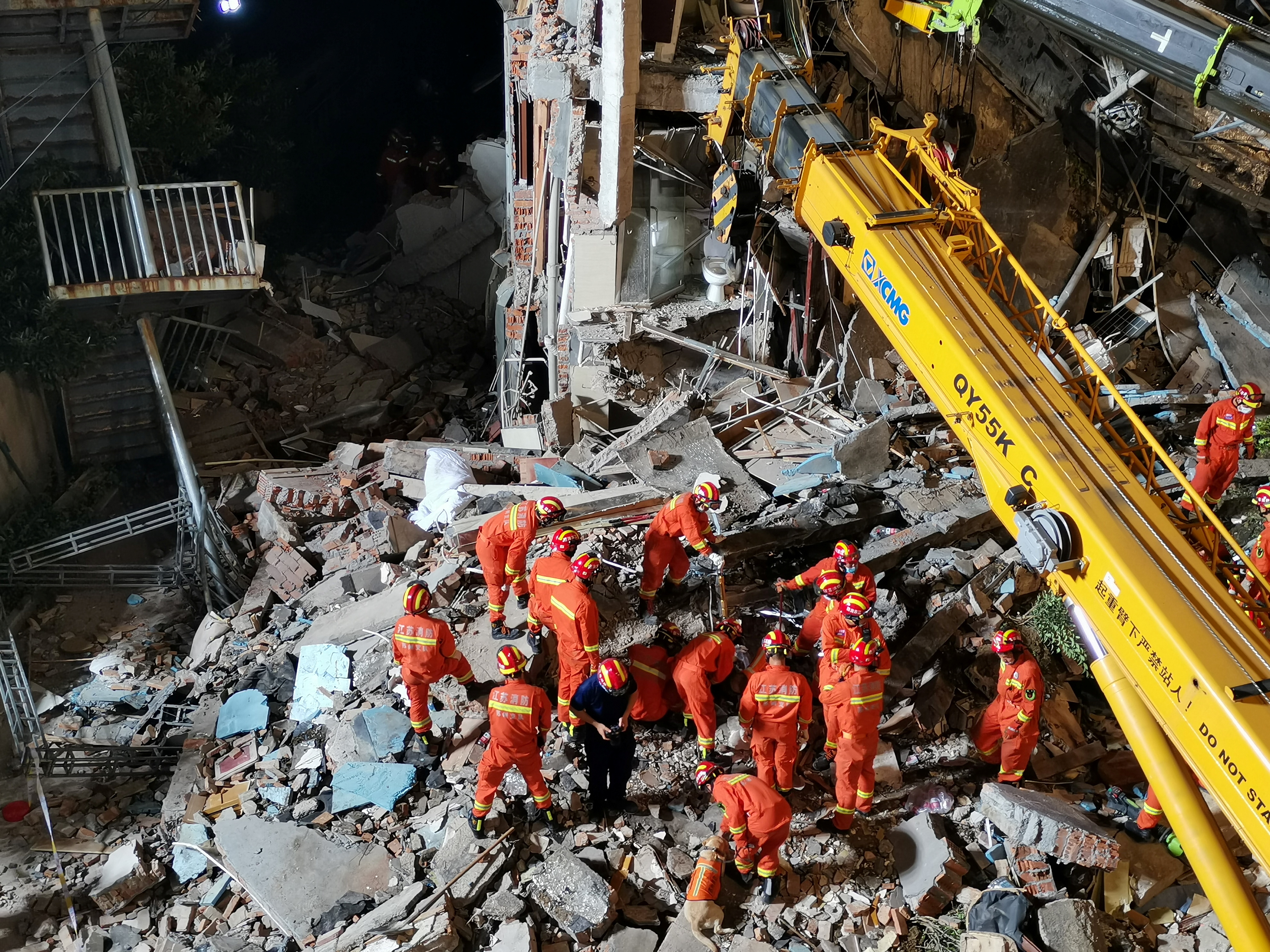 Rescue workers work next to a crane at the site where a hotel building collapsed in Suzhou