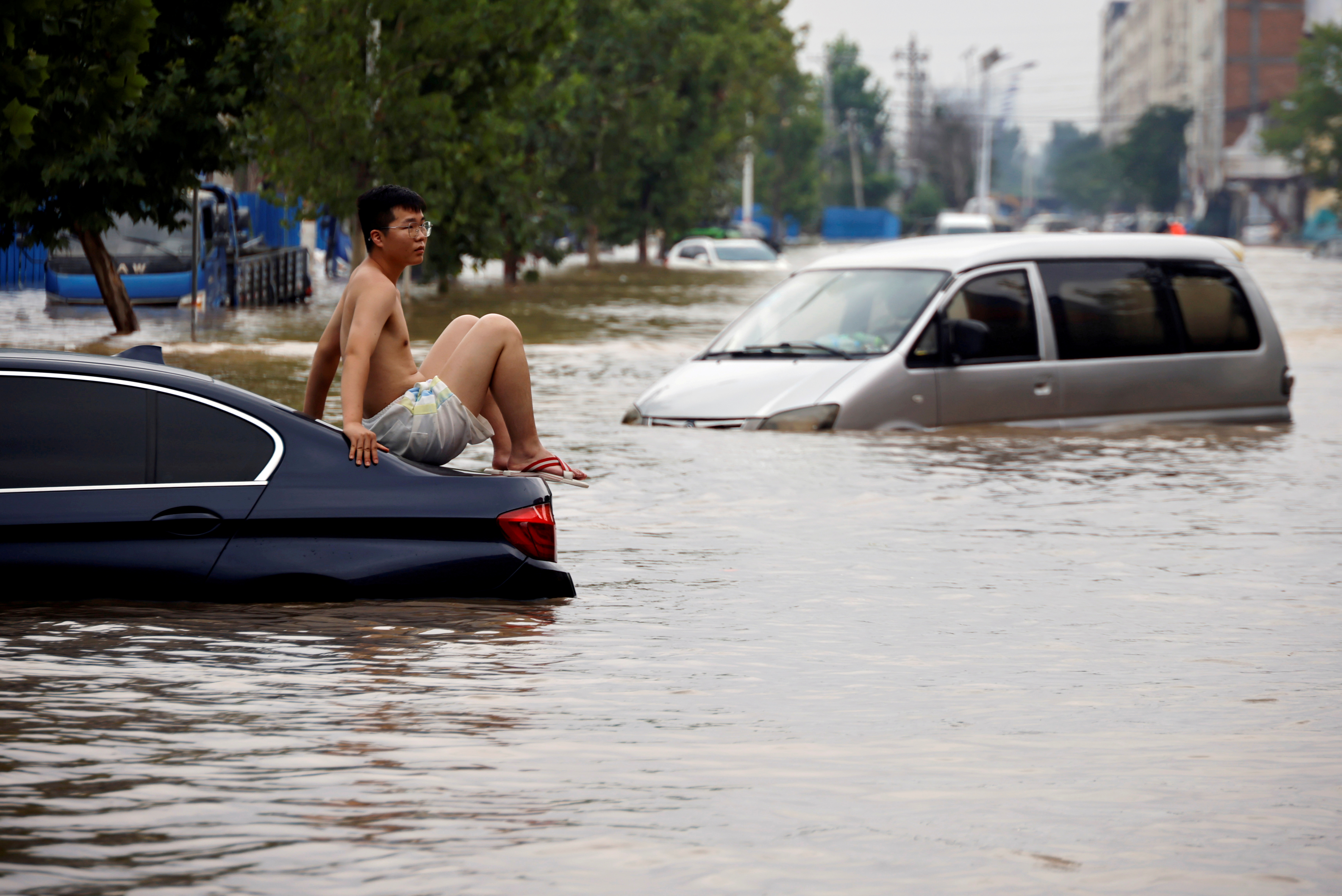 FILE PHOTO: Man sits on a stranded vehicle on a flooded road following heavy rainfall in Zhengzhou