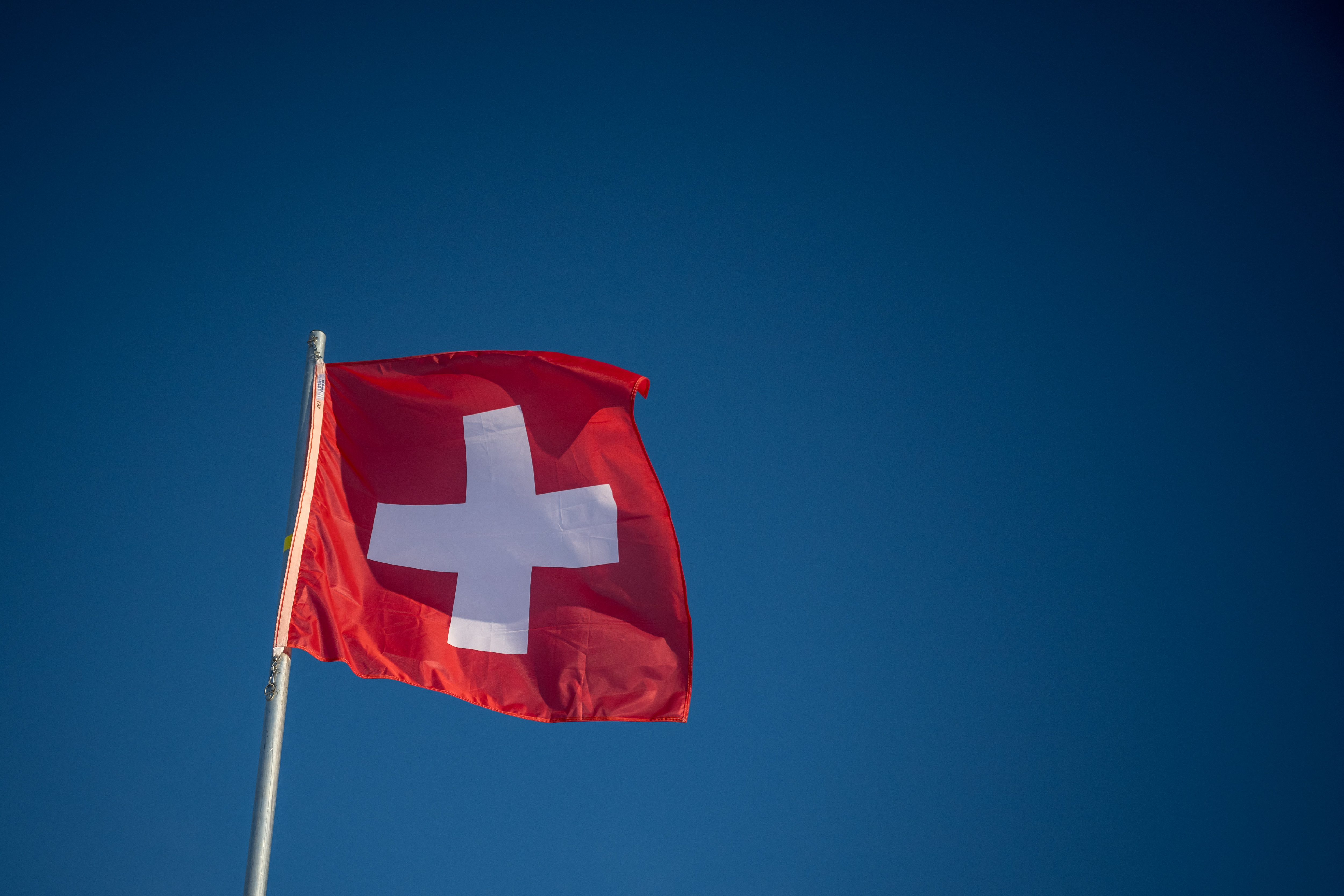 This photograph shows a Swiss flag waving in a blue sky in St.Moritz on December 21, 2024. (Photo by Fabrice COFFRINI / AFP)