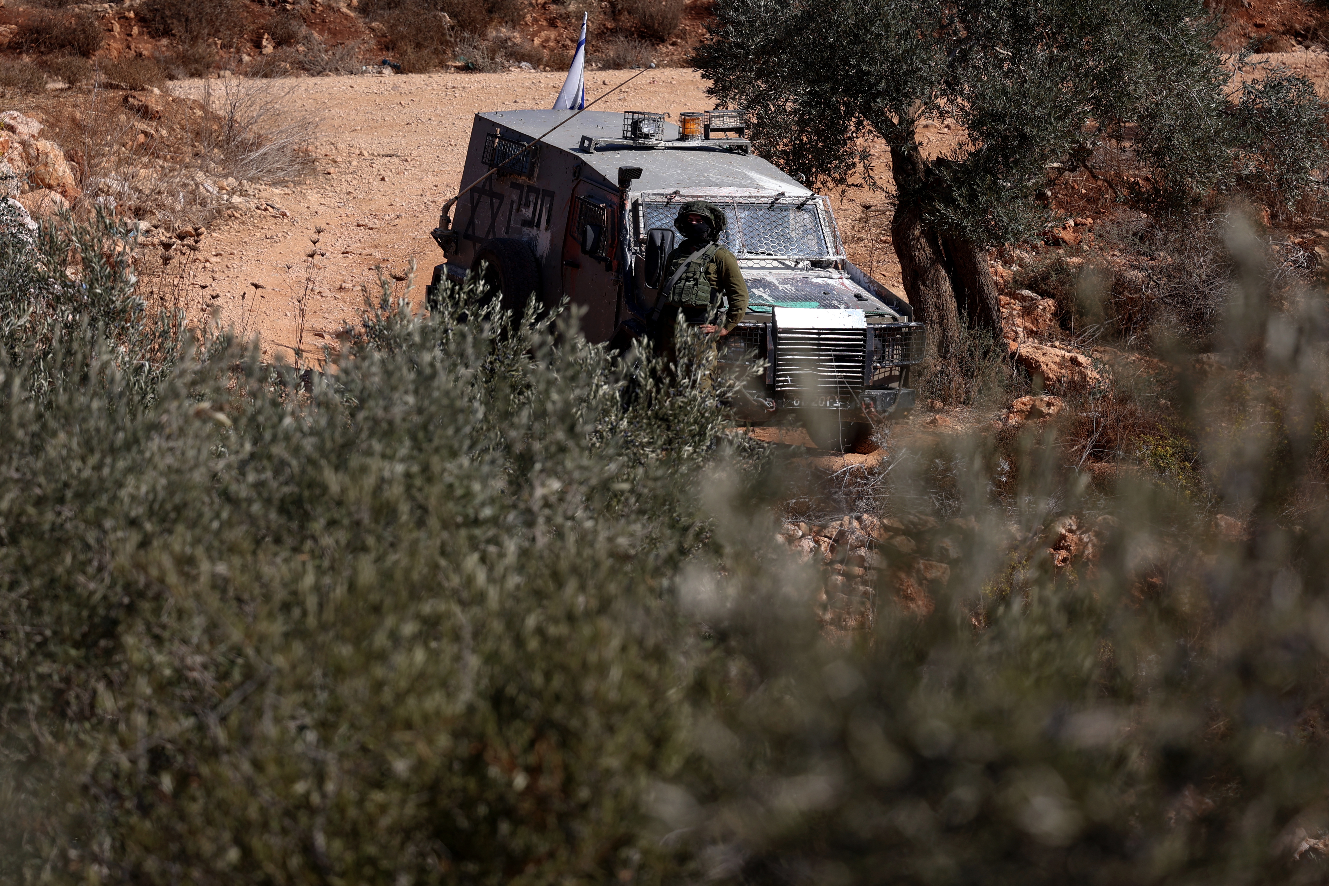 An Israeli military vehicle takes position along a dusty road in the olive groves after disrupting Palestinian farmers' olive harvest near the Israeli occupied Palestinian West Bank village of Turmus Ayya, near the city of Ramallah