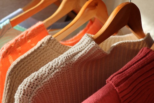 Warm sweaters on a wardrobe hanger on a light background. Autumn, winter clothes