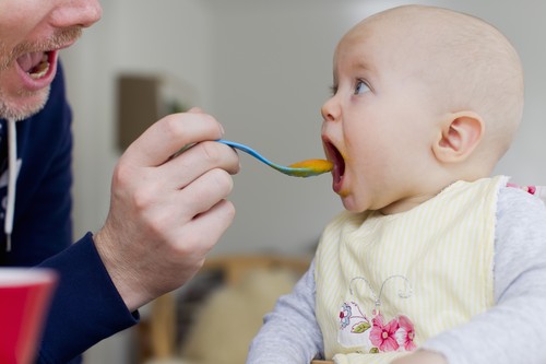 Father spoon feeding baby daughter