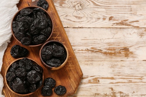 Bowls with dried prunes on white wooden background
